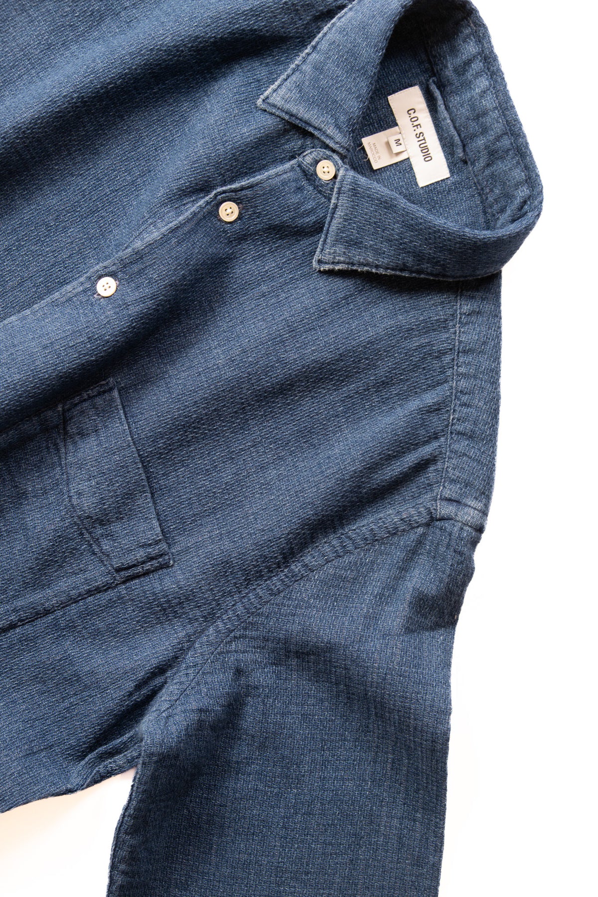 A close-up of a dark blue textured button-down shirt, showing the collar, and buttons.