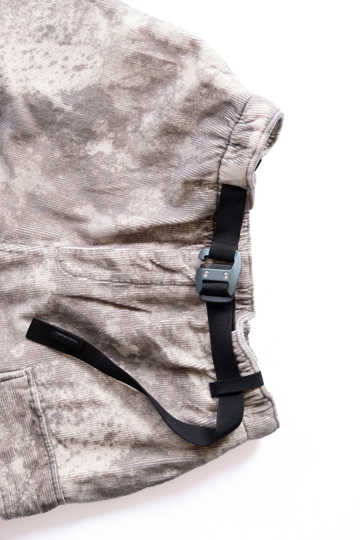 Close-up of a gray and beige winter camo cargo pant garment with a black adjustable strap and buckle, laid flat on a white background.