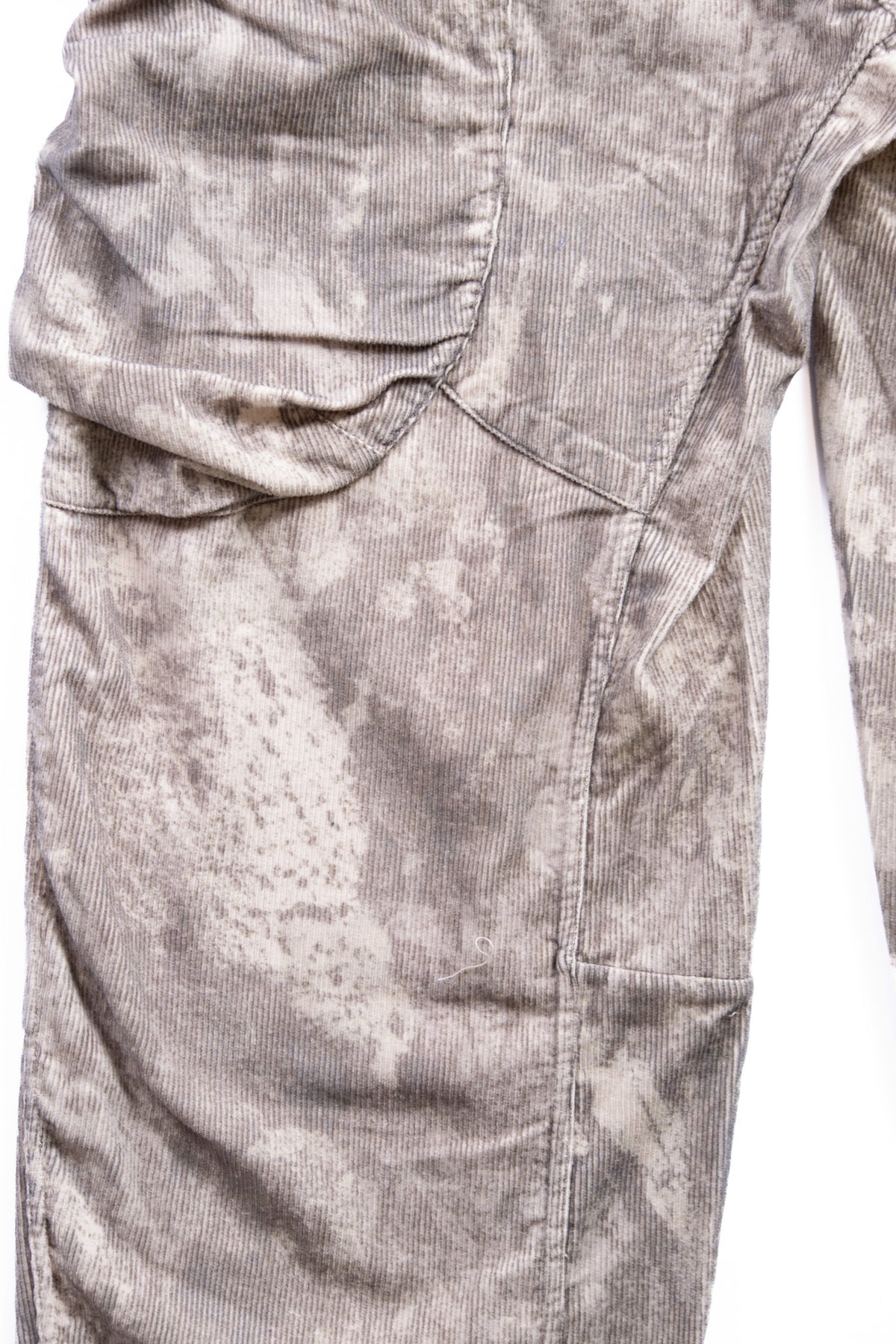 Close-up of a pair of corduroy cargo pants in a gray and beige winter camo pattern, showing the texture and fabric details.