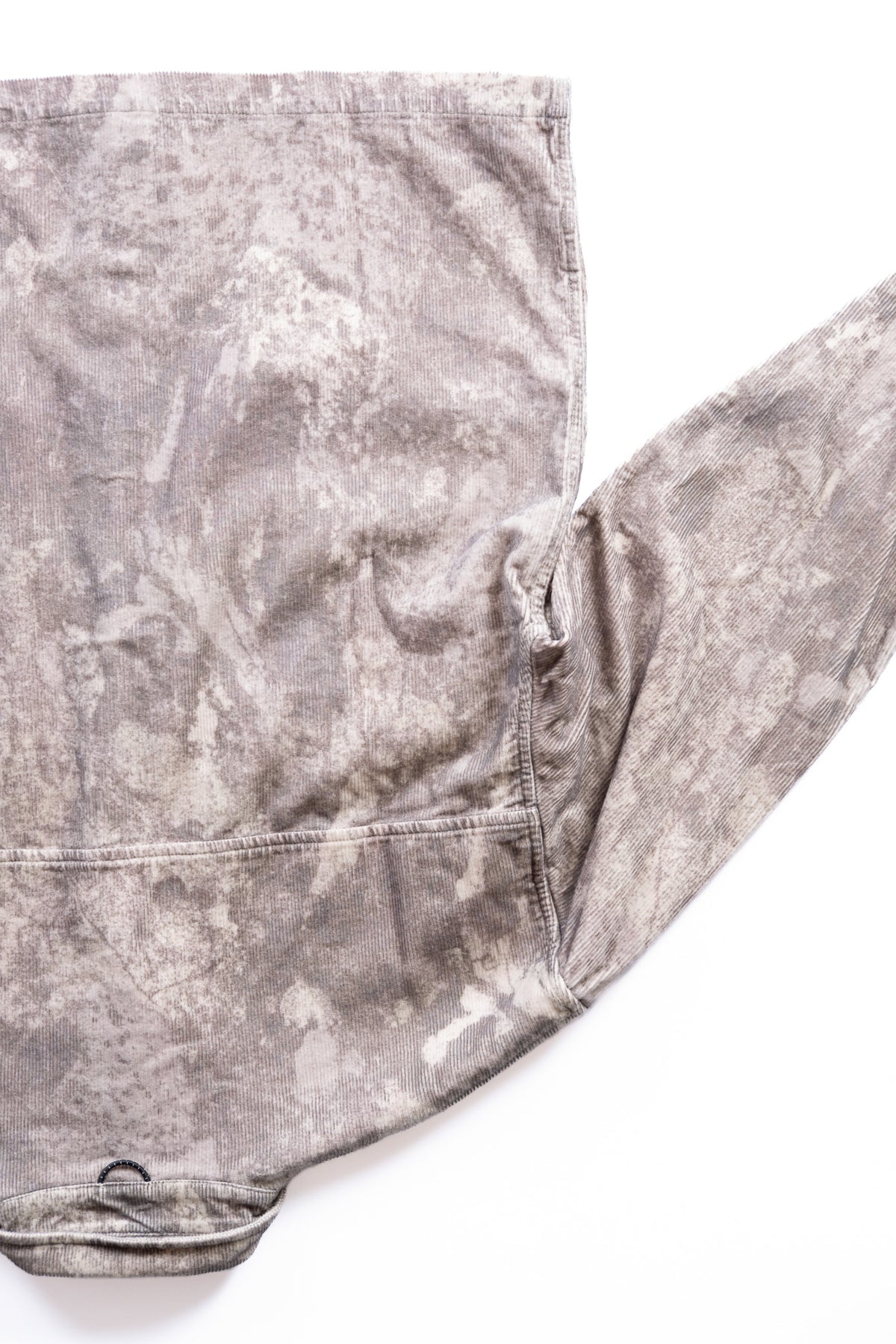 A close-up of a long-sleeve shirt laid flat on a white background, showing a mottled gray and off-white camouflage on corduroy fabric.
