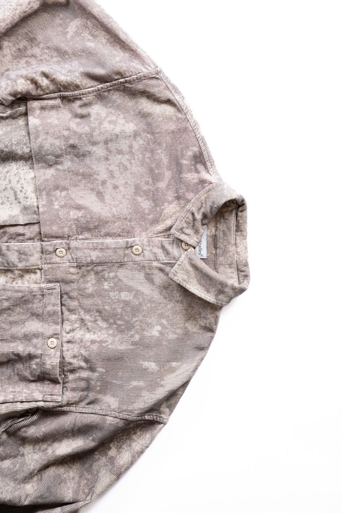 A close-up of a gray and brown winter camouflage, corduroy button-up shirt laid flat on a white background.