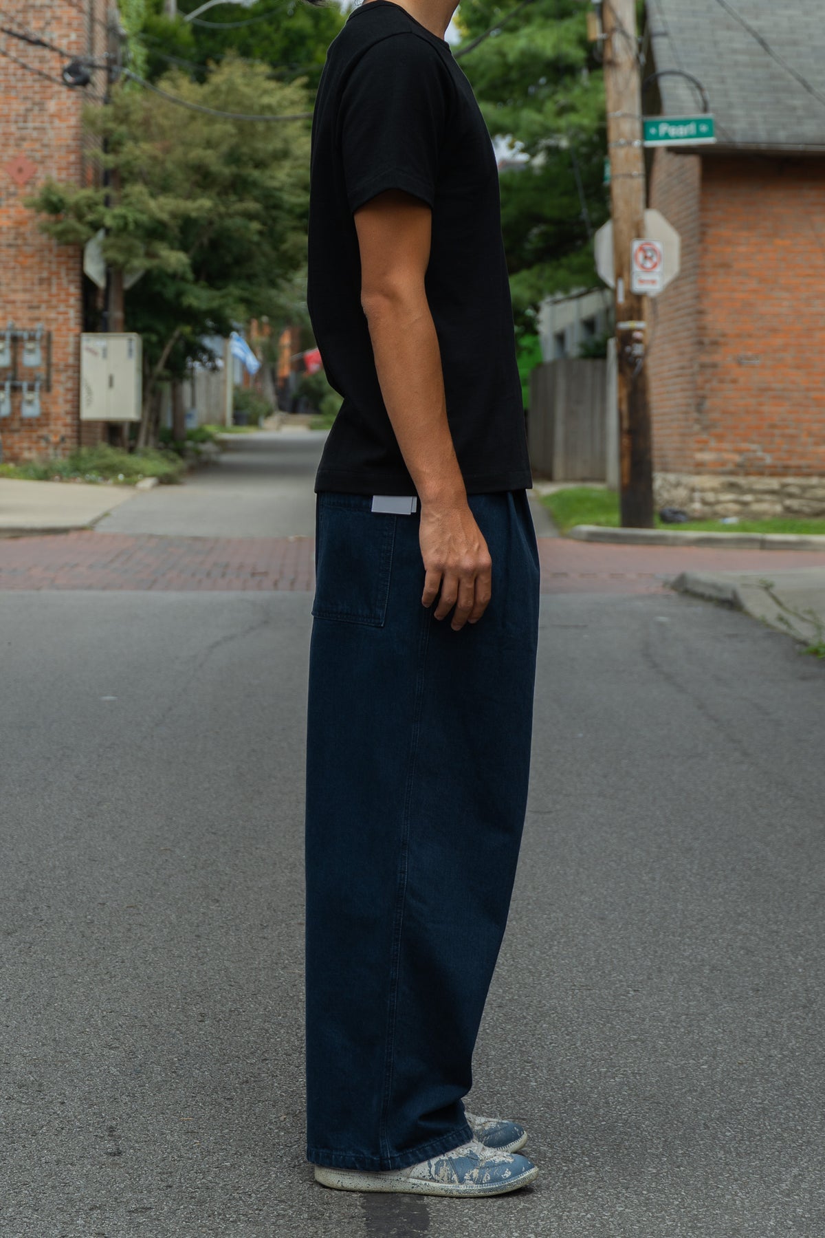 A person standing on a street wearing a black short-sleeve t-shirt, dark navy blue wide-leg pants, and light blue sneakers.