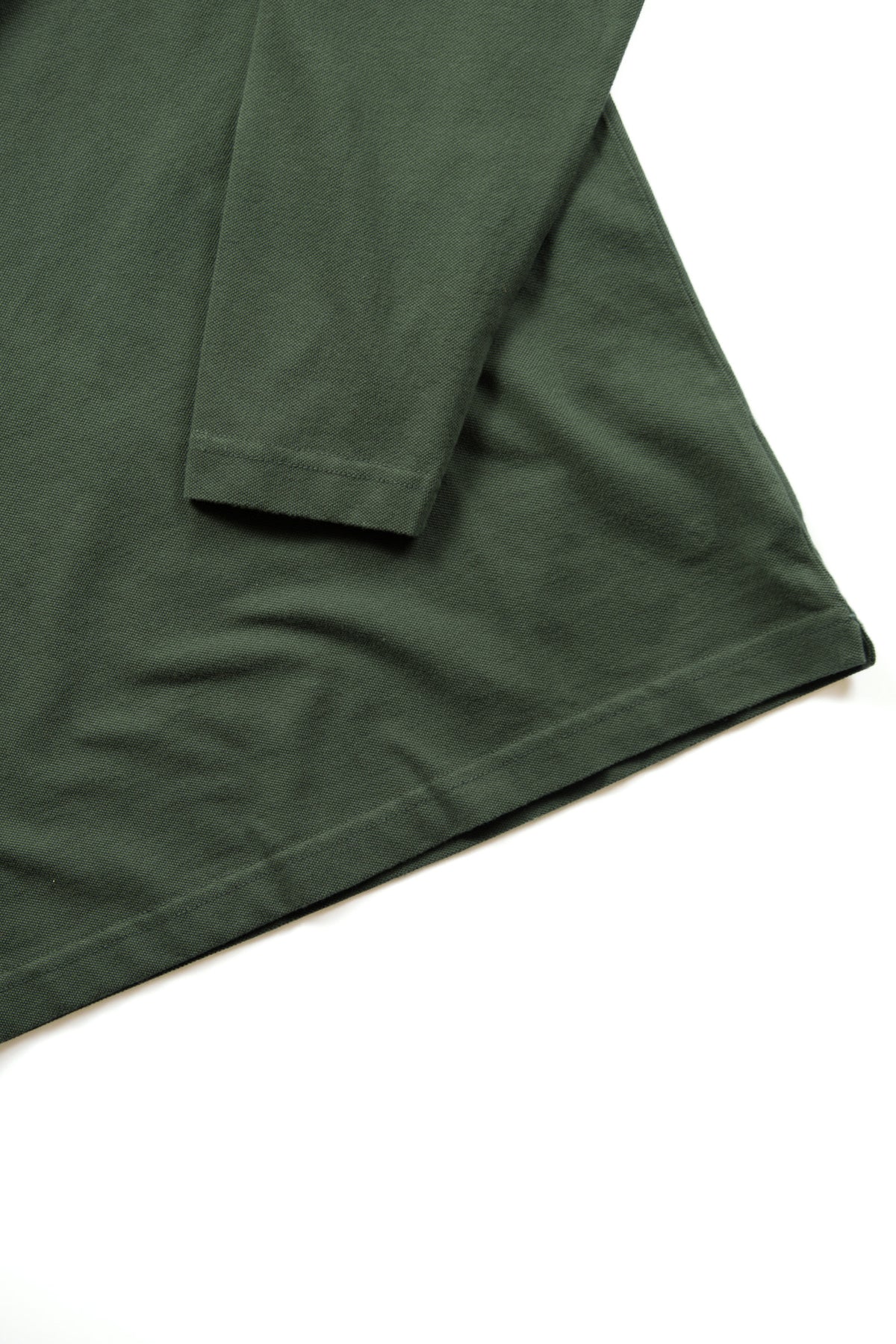 A close-up of a dark green long-sleeve shirt, showing the fabric texture and hem against a plain white background.
