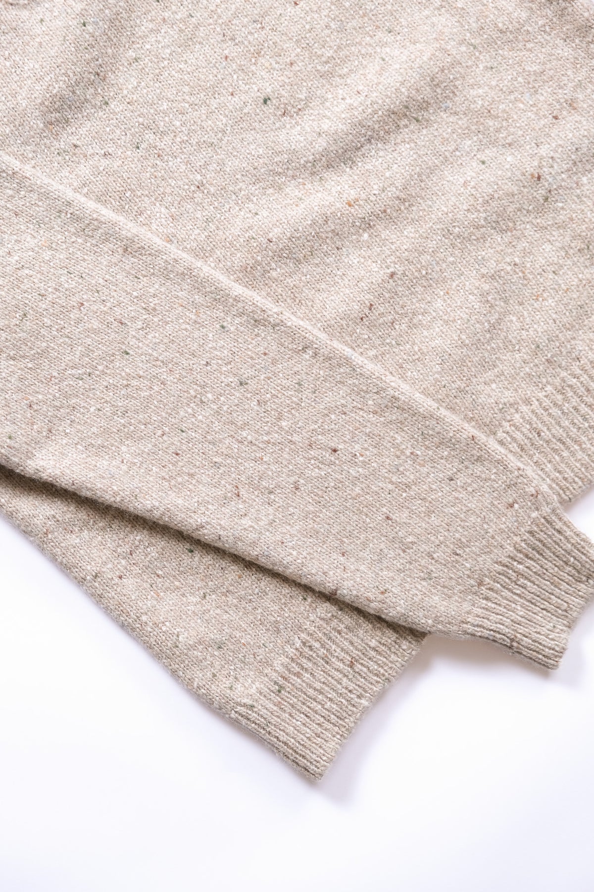 Close-up of a taupe knit sweater with subtle flecks and ribbed cuffs, laid flat on a white background.