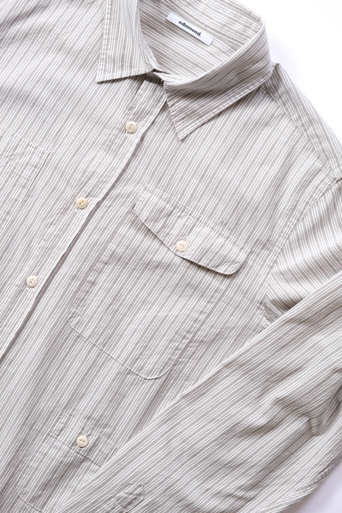 A close-up of a long-sleeve button-up shirt with fine vertical stripes in grey and white, featuring a chest pocket and cream-colored buttons.