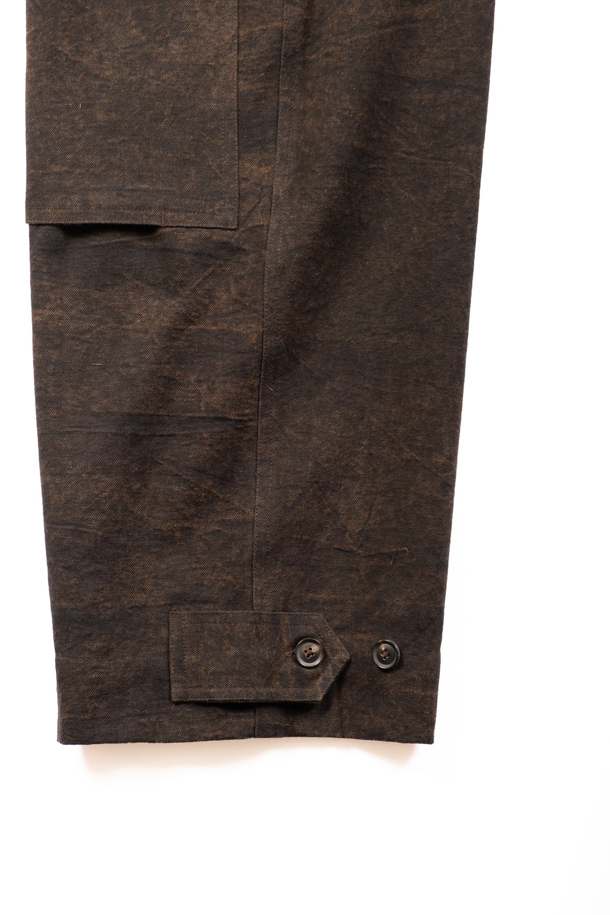 Close-up of a dark brown textured fabric garment, showing double knee and buttoned hem detail on a white background.