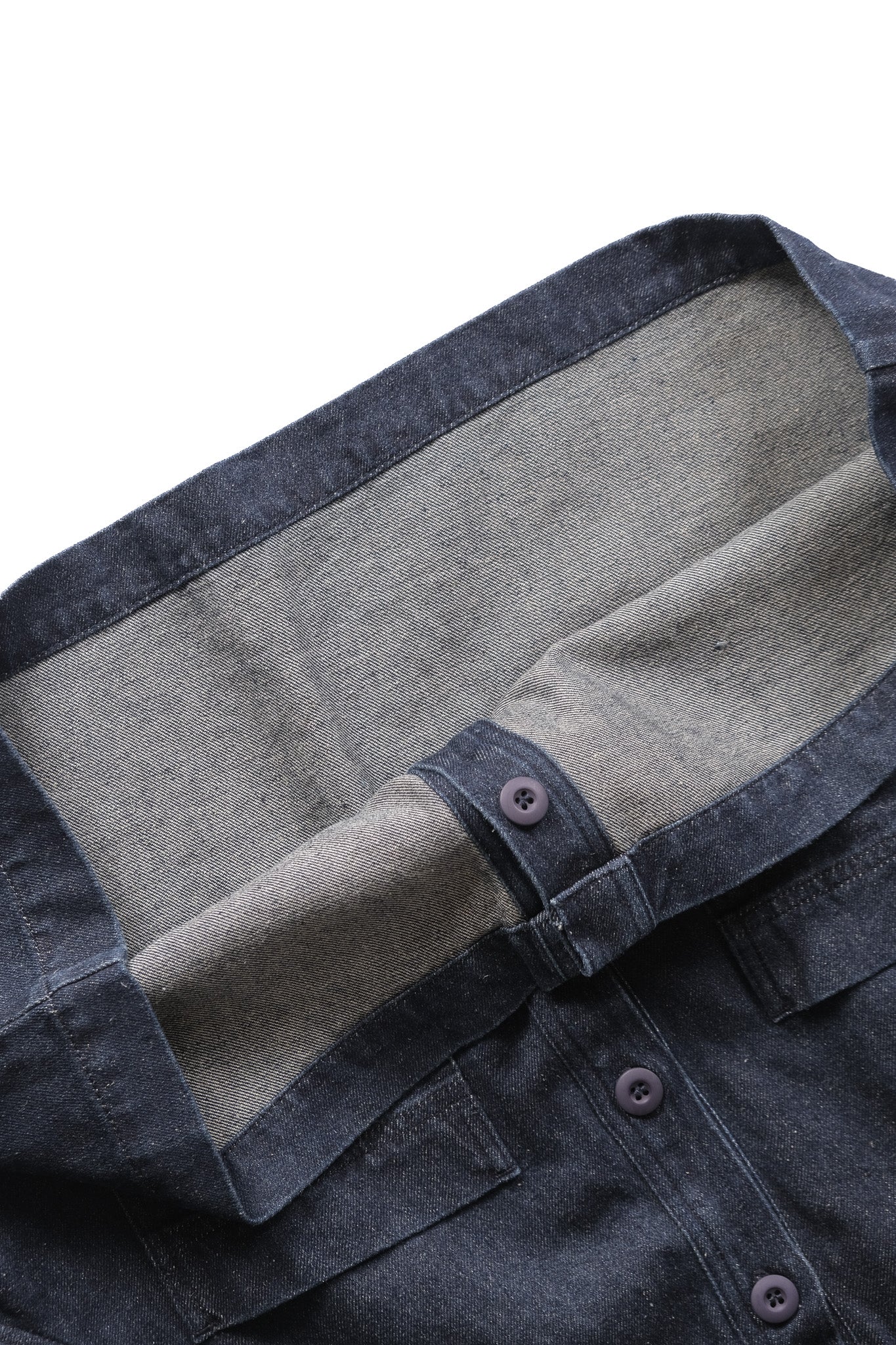Close-up of a dark indigo denim shirt with a contrasting inner lining and button details, set against a plain white background.