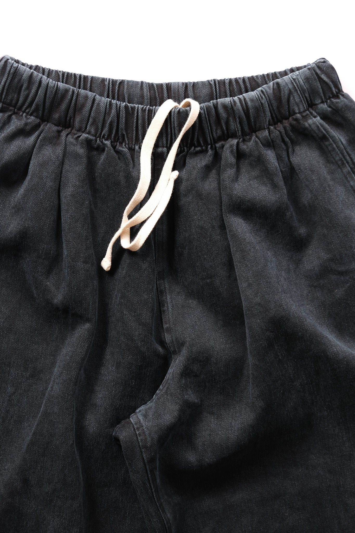 Close-up of black drawstring pants showing the elastic waistband and a cream-colored drawstring against a white background.