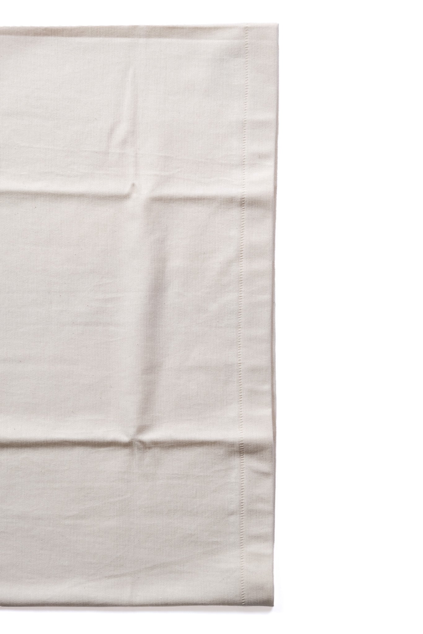 A close-up of a light beige or off-white fabric surface with visible folds and a stitched edge, shown against a white background.