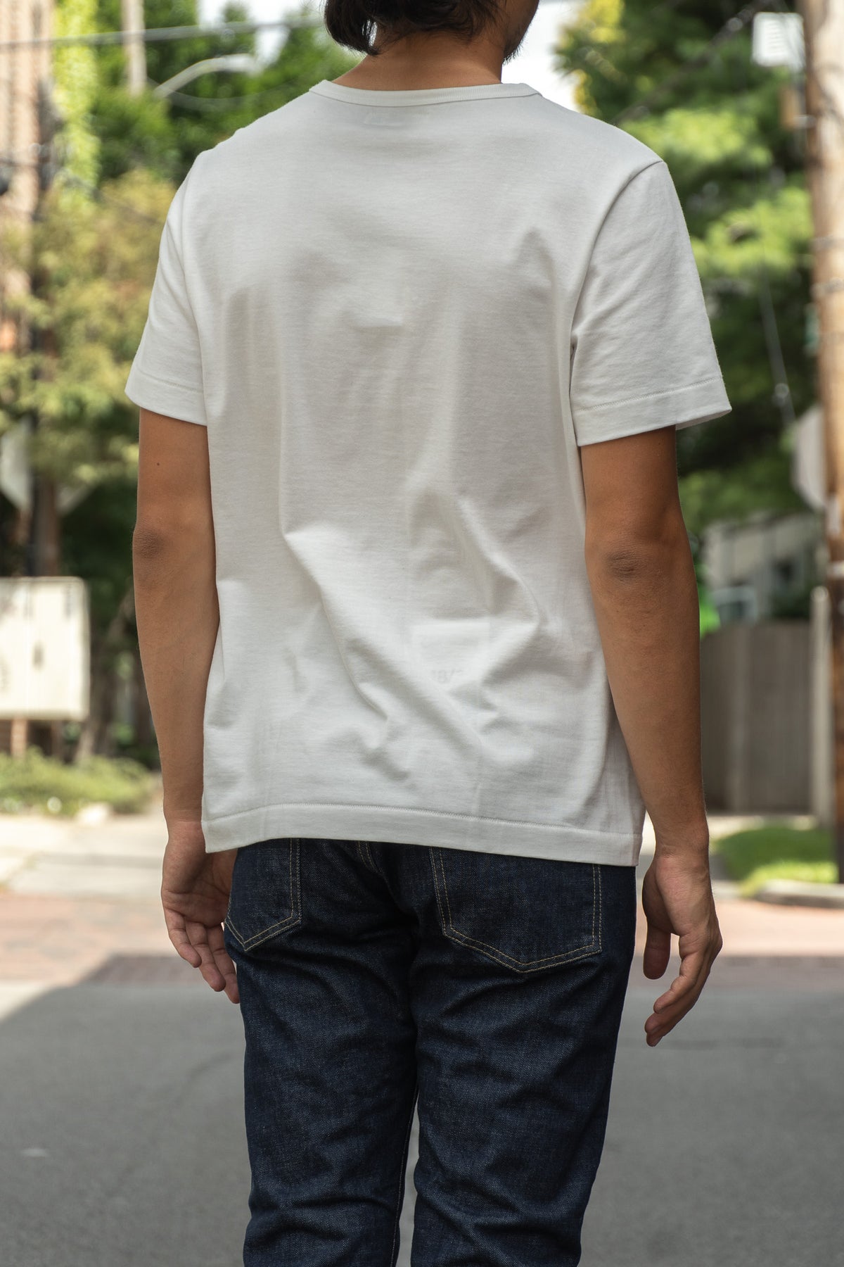 A person viewed from behind wearing a plain white short-sleeve crewneck t-shirt and dark blue jeans, standing outdoors
