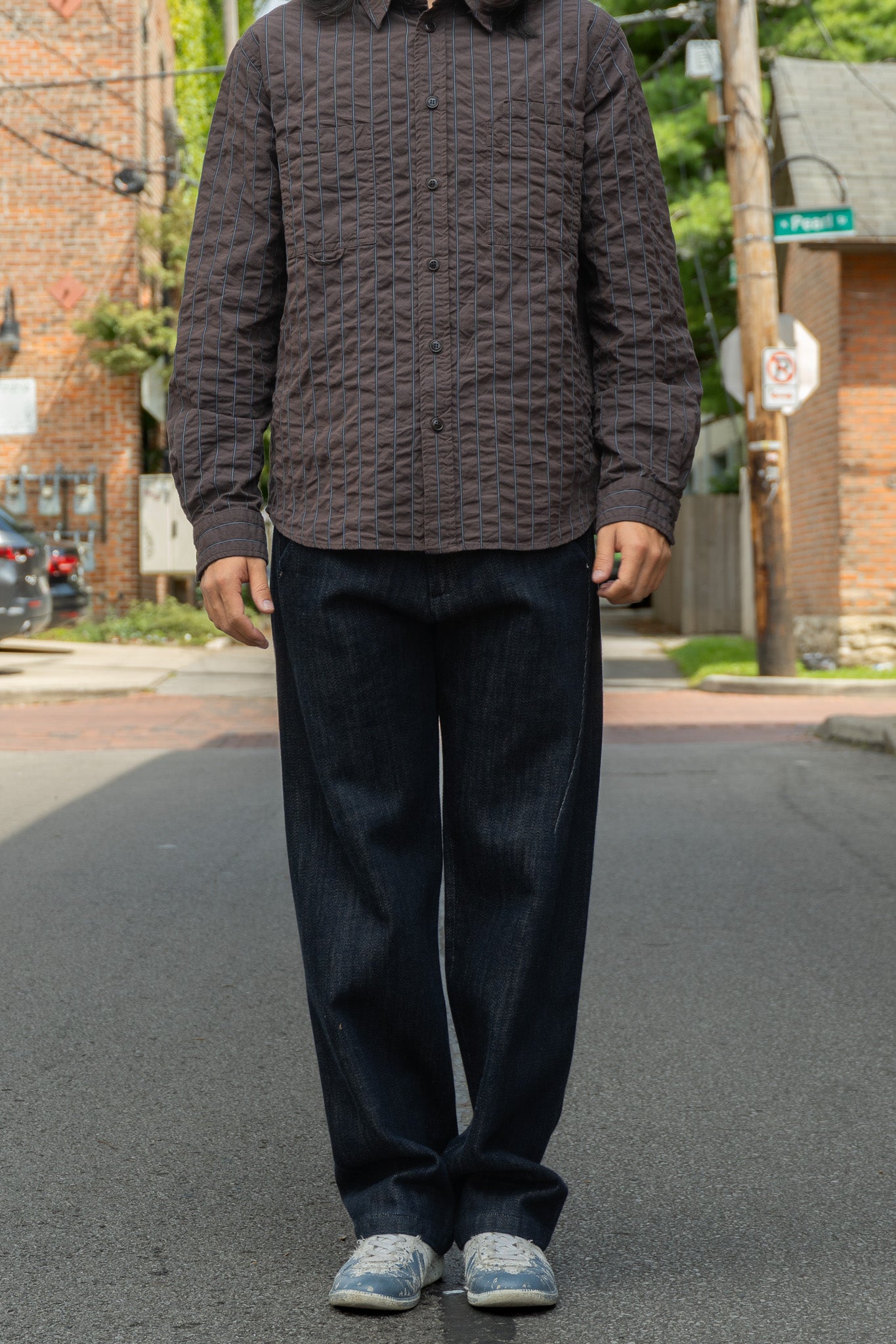 A person standing on an outdoor street wearing a dark brown seersucker button-up shirt and dark blue jeans.