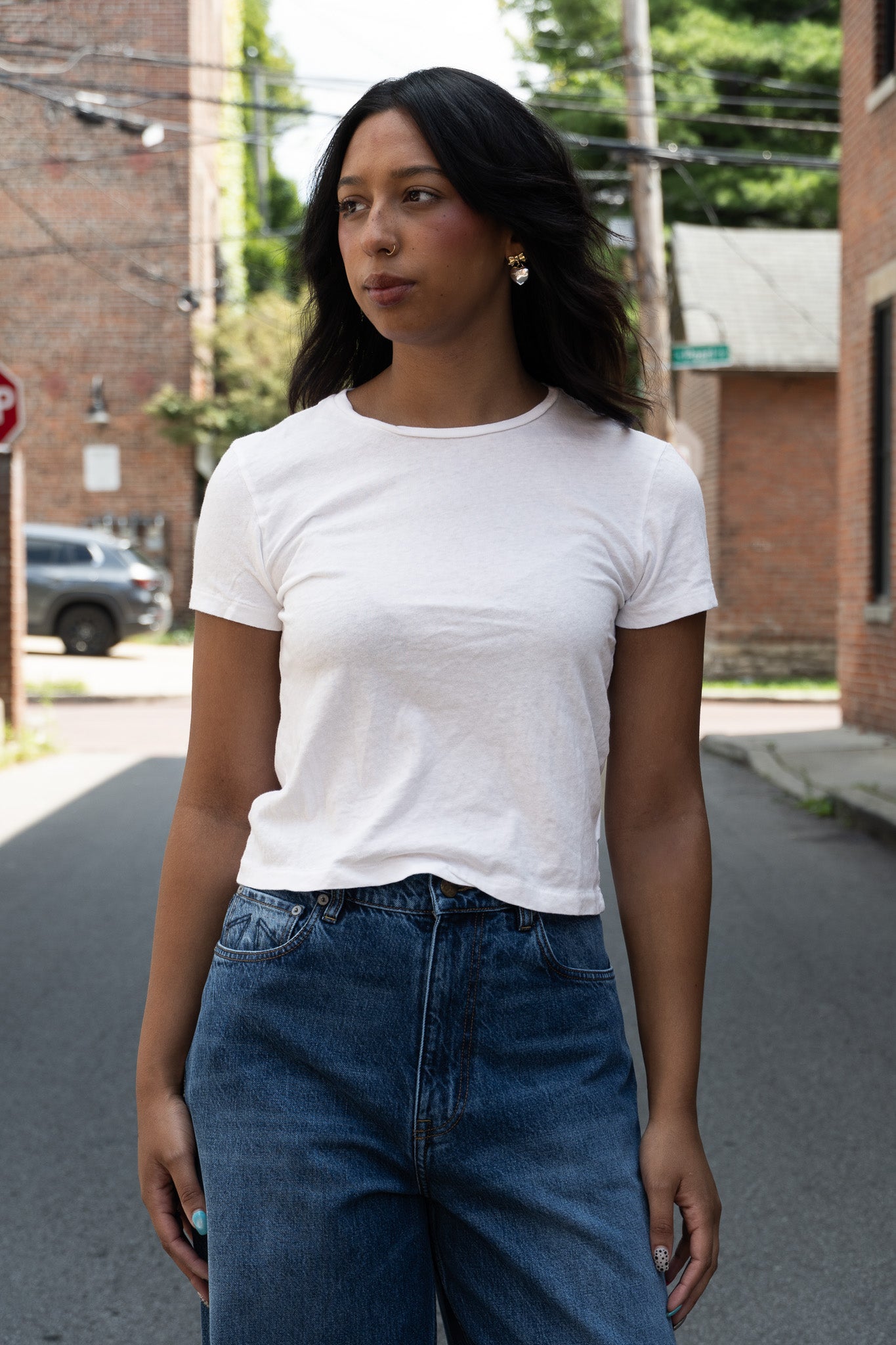 A woman wearing a plain white short-sleeve crewneck t-shirt and blue jeans standing in the street.