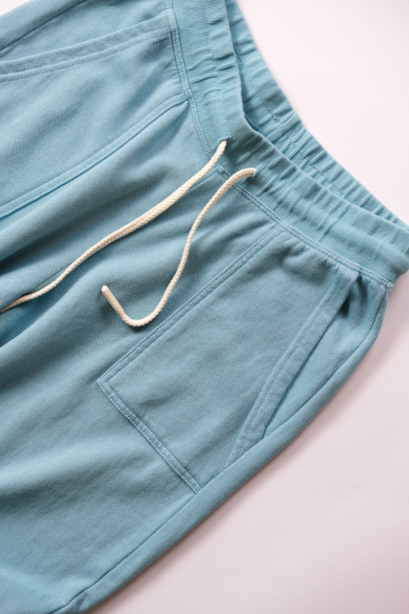 Close-up of a pair of light blue sweatpants featuring a cream-colored drawstring and a side pocket