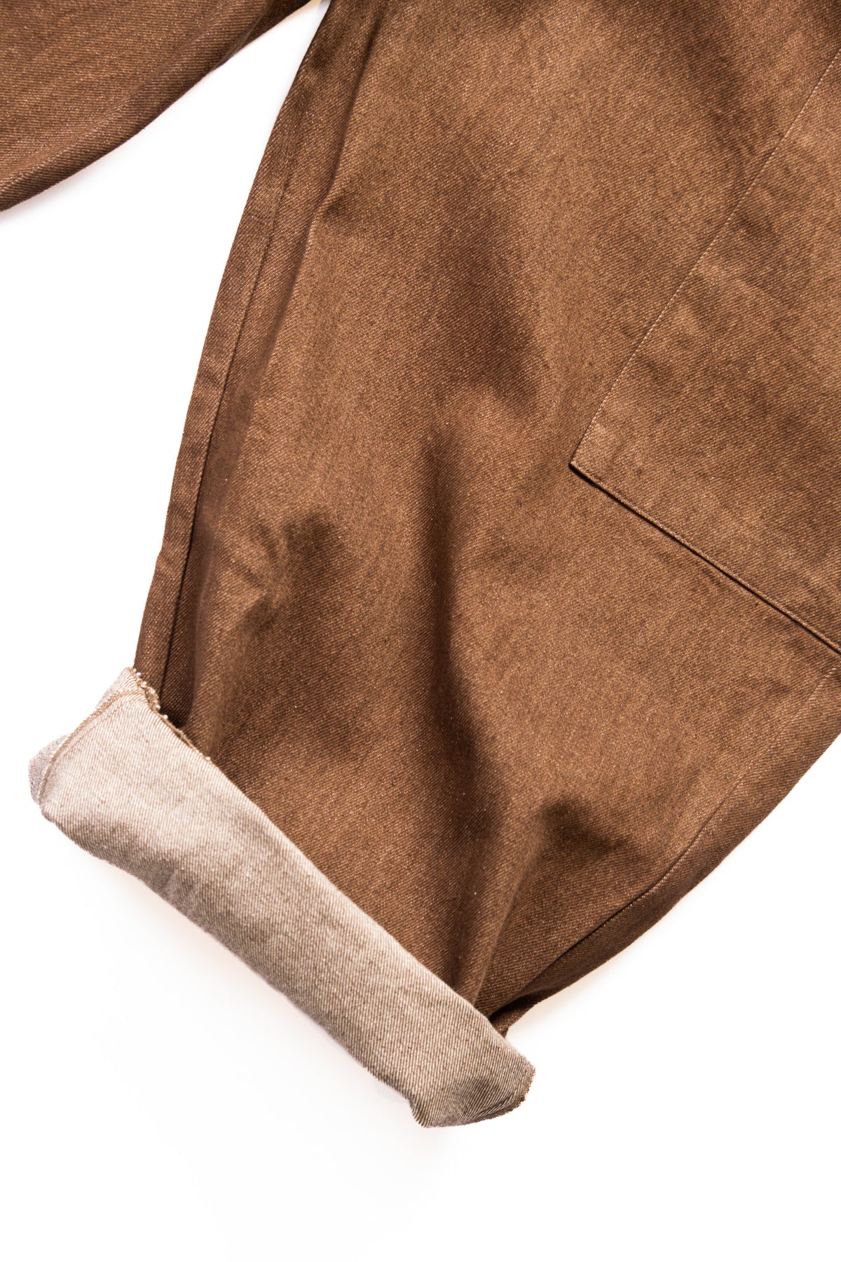 Close-up of a brown denim pants with a rolled cuff showing a light beige reverse photographed on a white background.