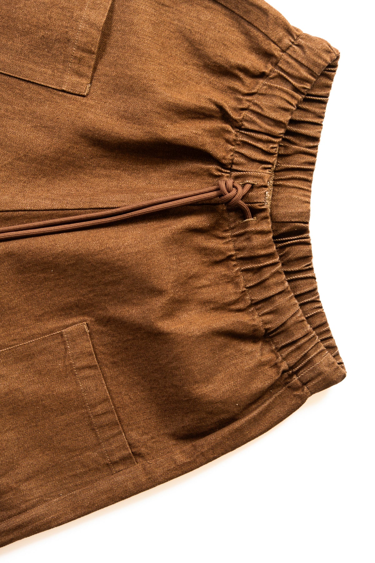 Close-up of brown drawstring pants showing the elastic waistband and side pocket on a white background.
