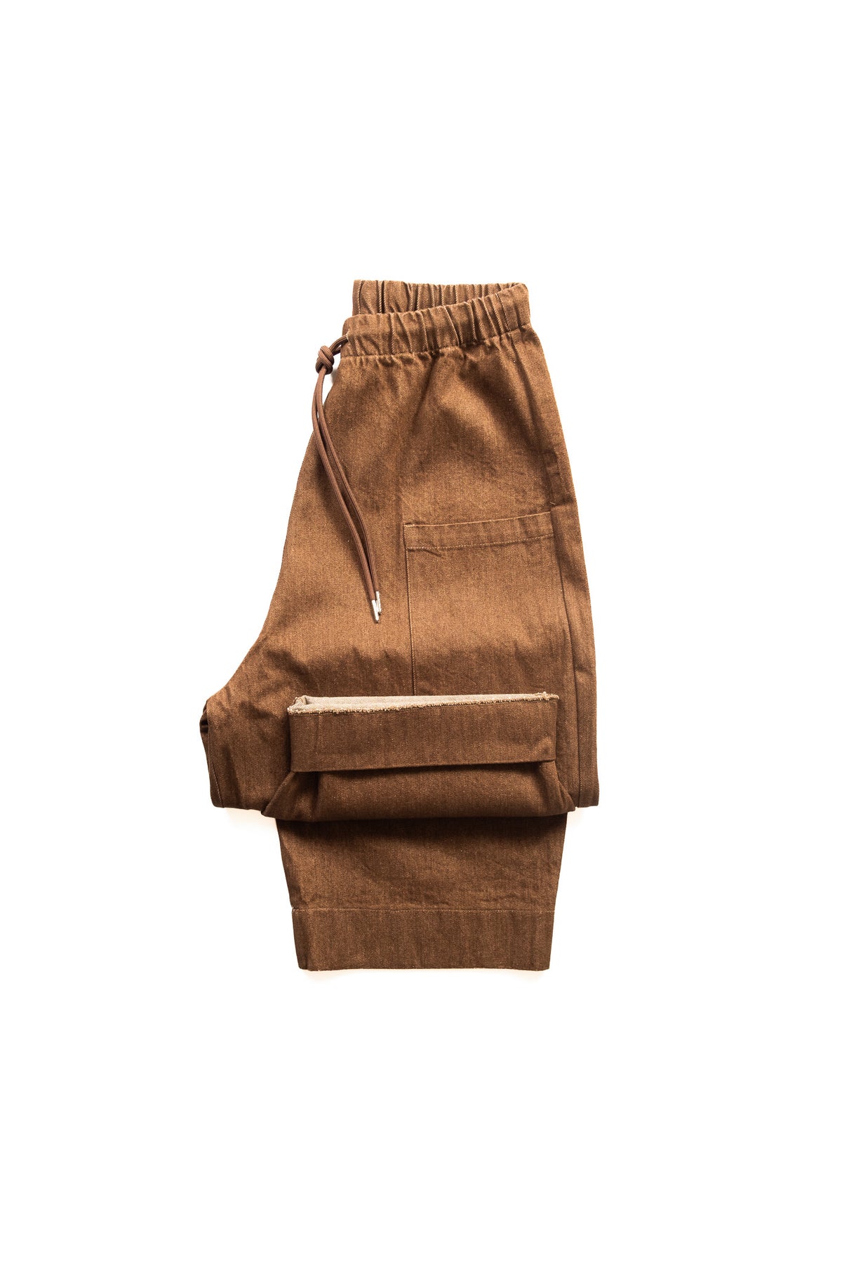 A pair of brown denim trousers with an elastic waistband, drawstring, and a large front flap pocket, shown folded on a white background.