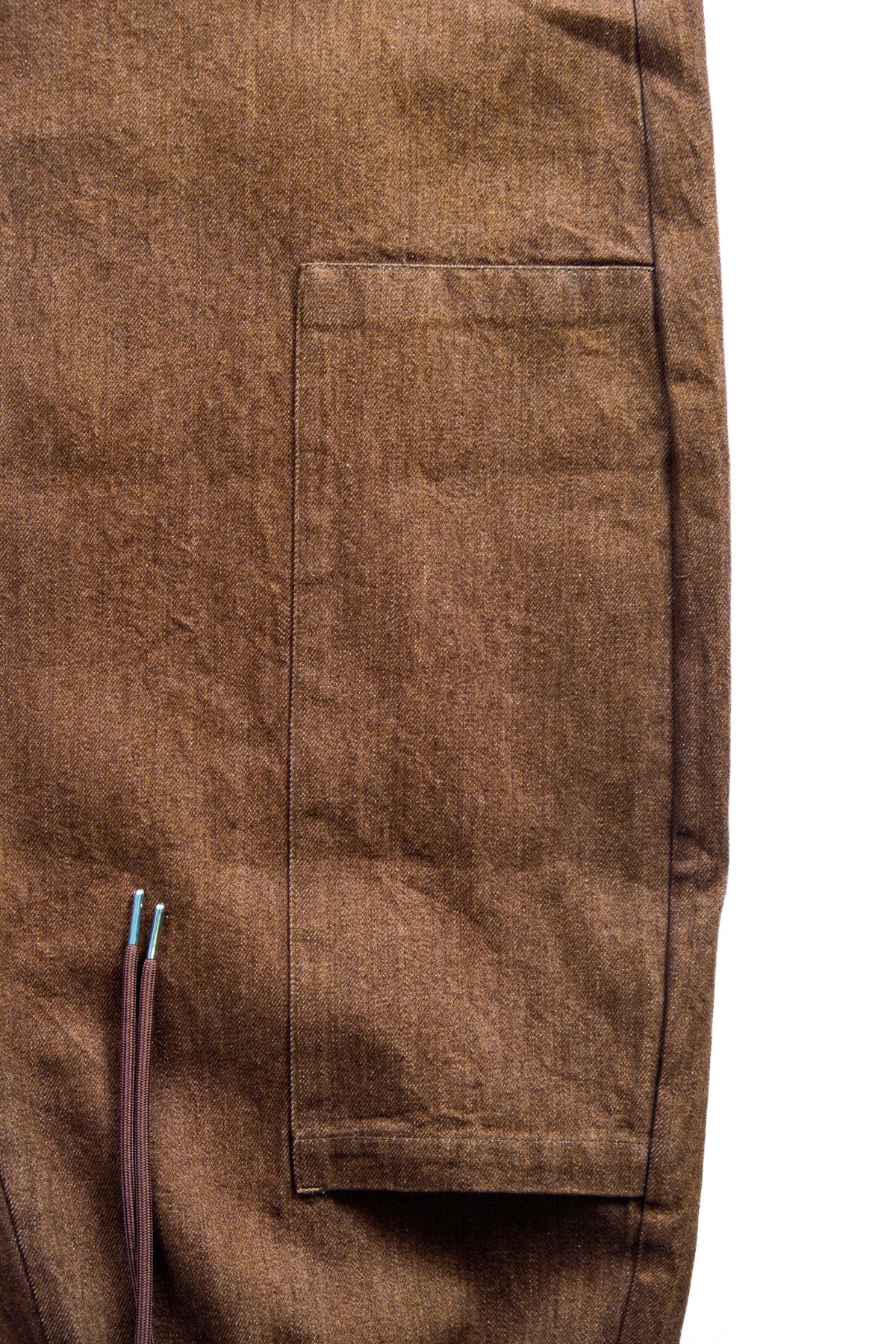 Close-up of a brown textured fabric garment showing a rectangular patch pocket and a small portion of a drawstring against a white background.