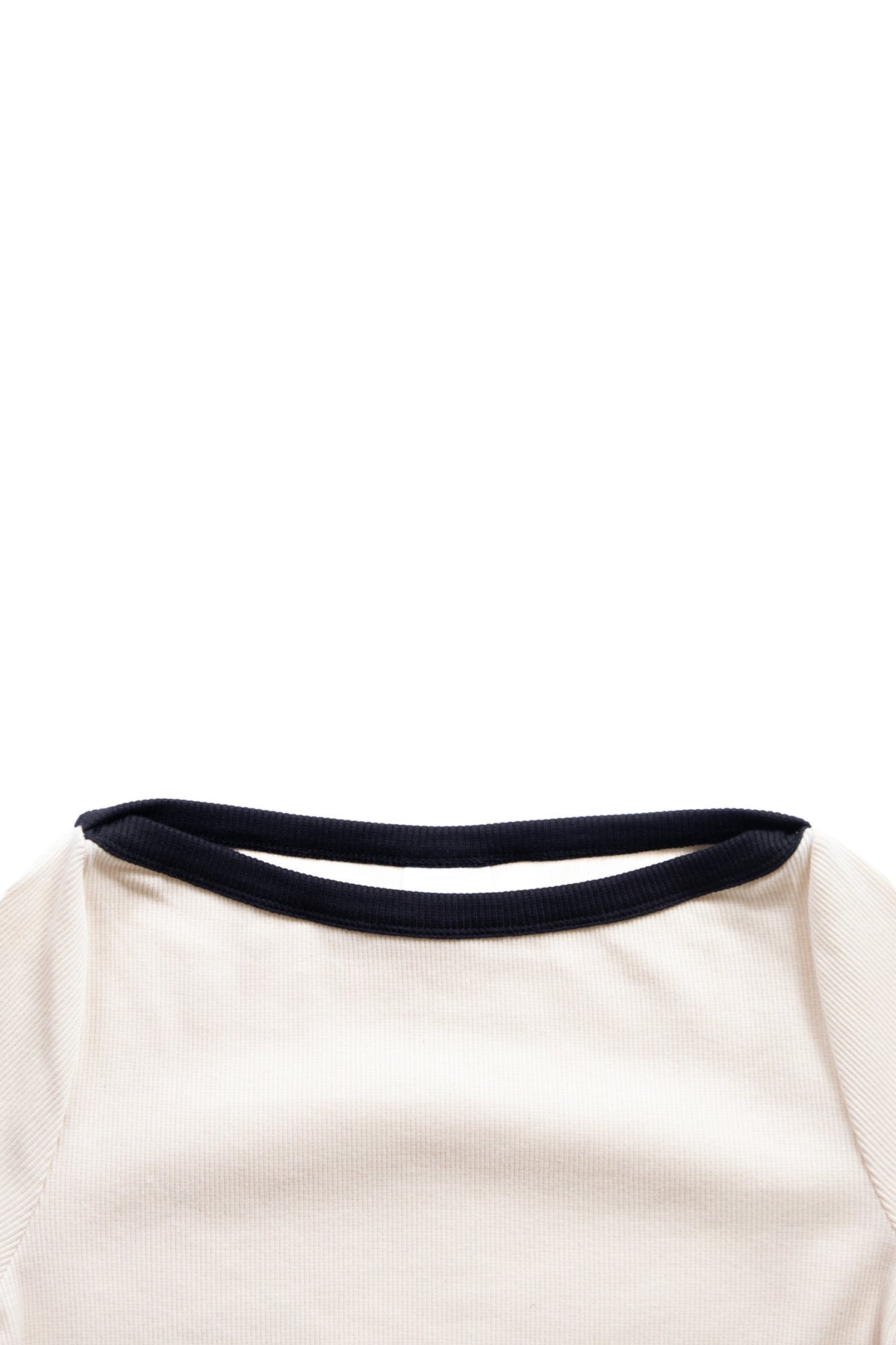 Close-up of a cream-colored ribbed knit top with a contrasting black crew neck trim, shown against a plain white background.
