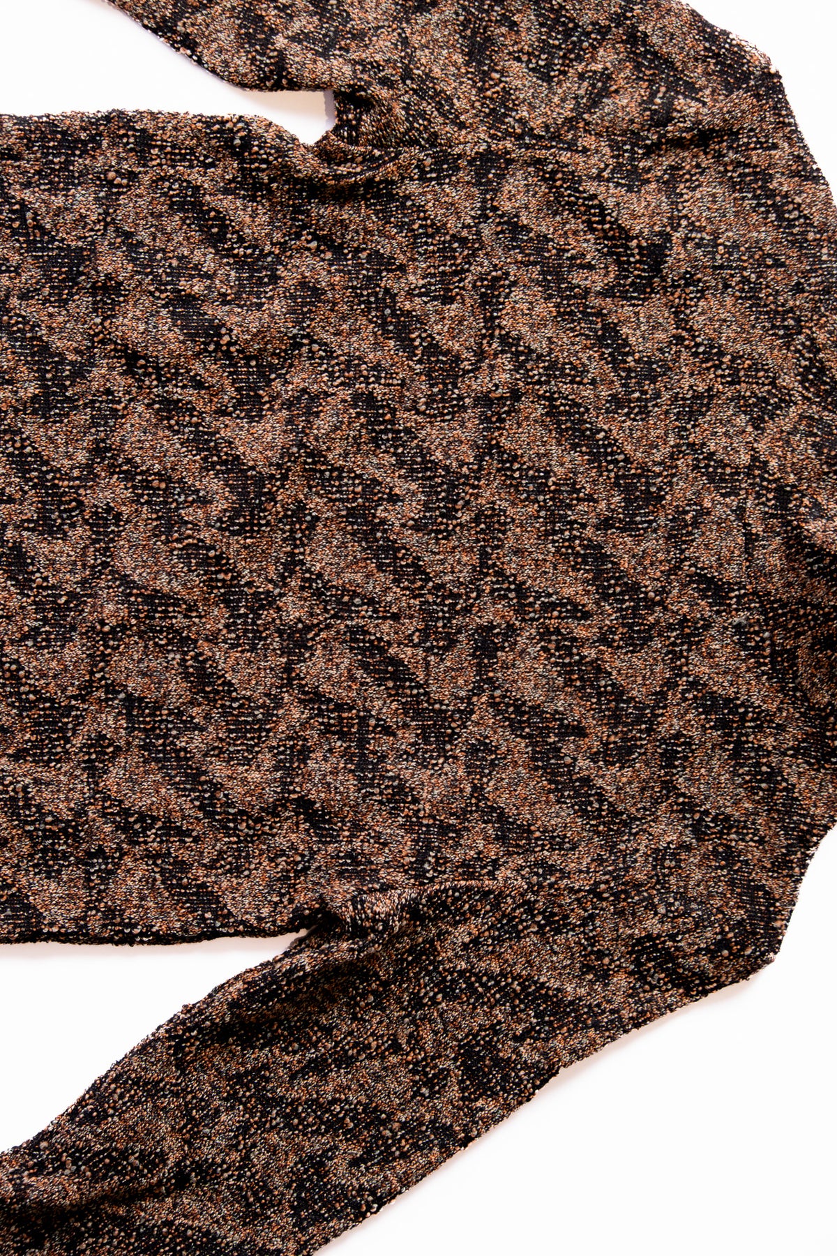 A close-up of a textured knit fabric with an interlocked pattern in brown, black, and beige, laid flat on a white background.