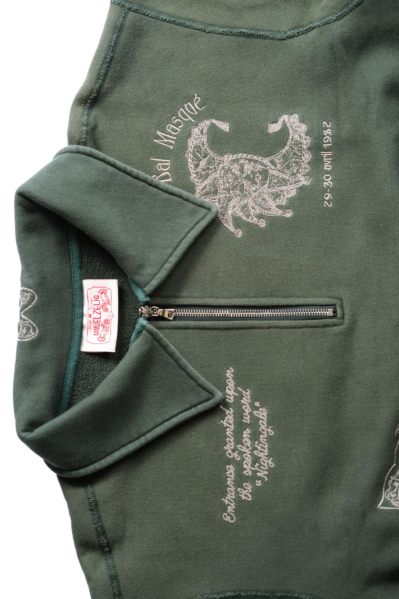 Close-up of an emerald green zippered sweatshirt featuring embroidered white graphics and text.