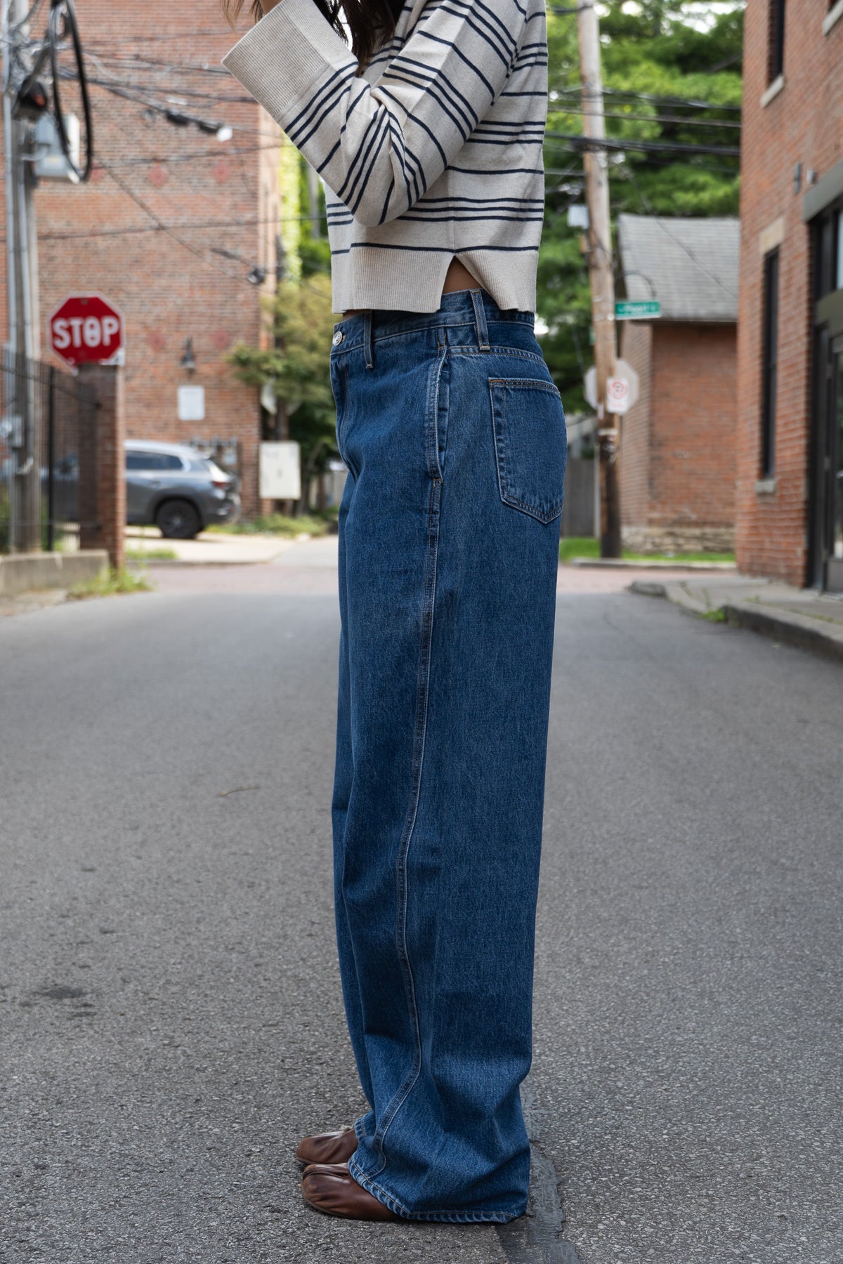 A person standing on a street wearing a cream and navy striped long-sleeve crop top and high-waisted, wide-leg blue denim jeans.