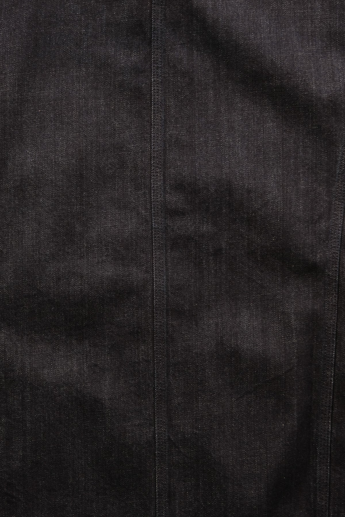 A close-up of dark denim fabric with a visible vertical seam and fine woven texture.