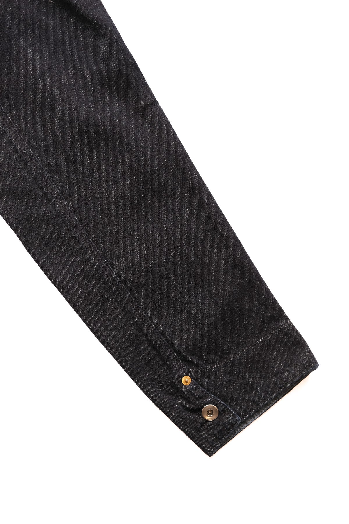 Close-up of a dark washed denim jacket sleeve with a buttoned cuff detail, shown against a plain white background.