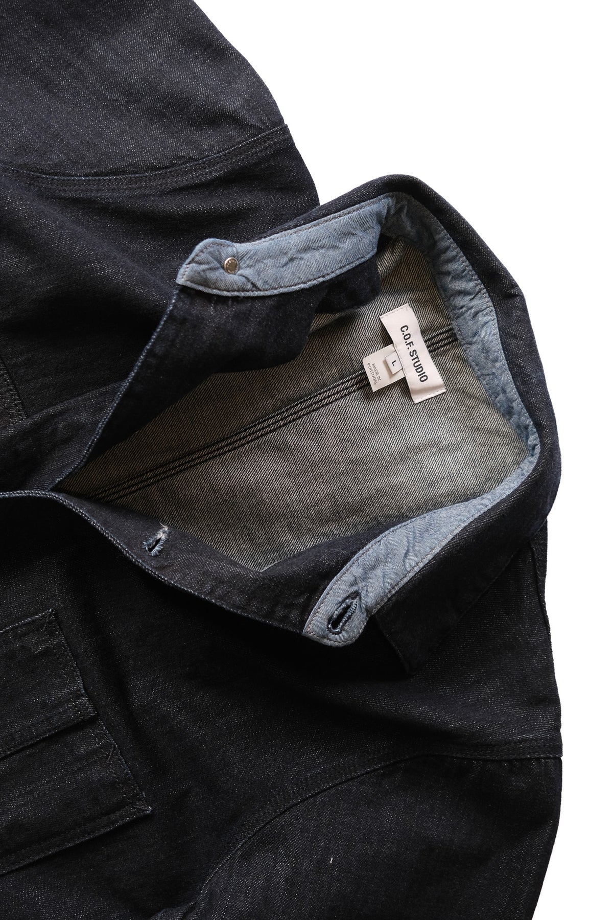 Close-up of a dark indigo denim jacket collar laid on flat on a white background.