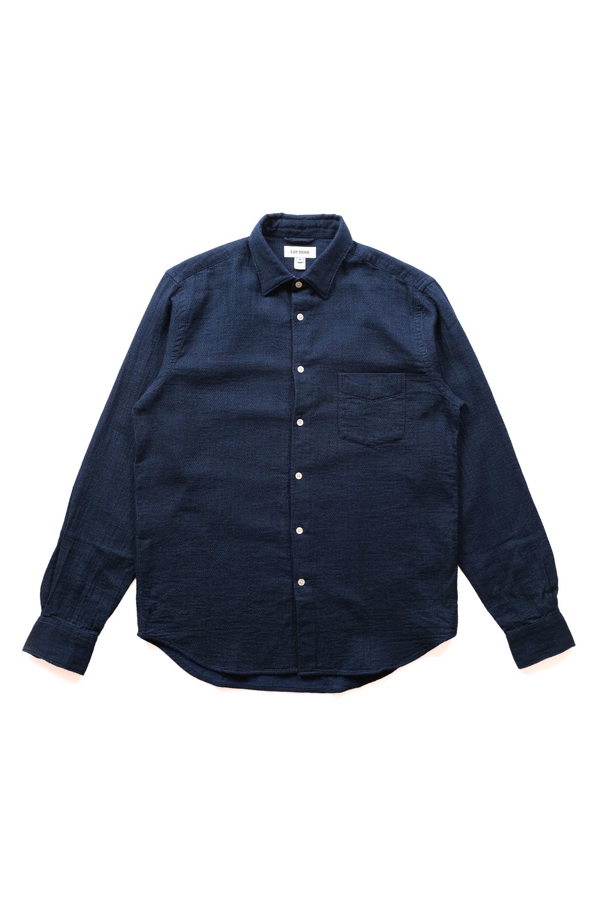 A dark indigo blue long-sleeve button-up shirt with a single chest pocket, laid flat against a solid white background.