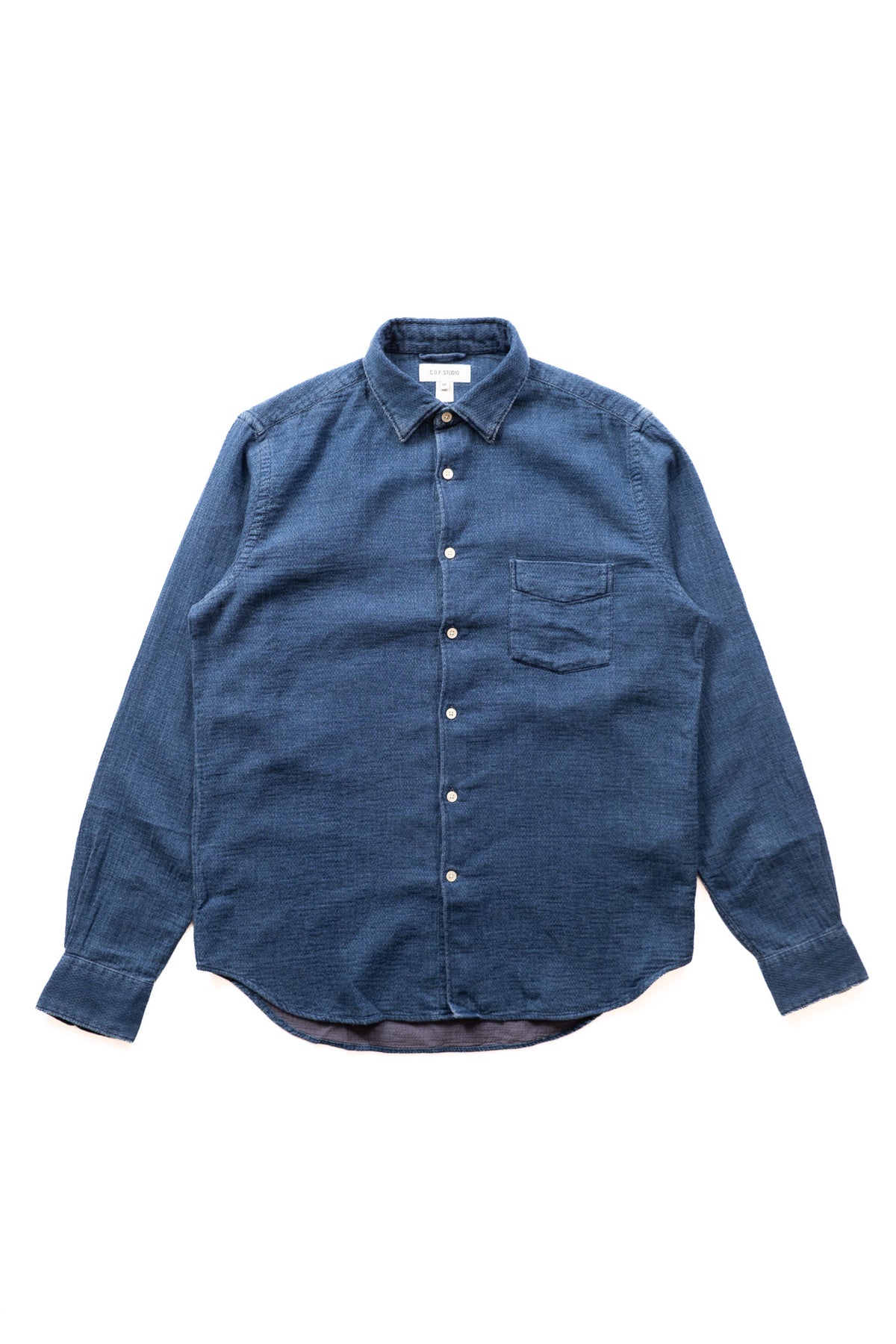 A washed indigo blue textured button-down shirt with a single chest pocket, laid flat on a white background.