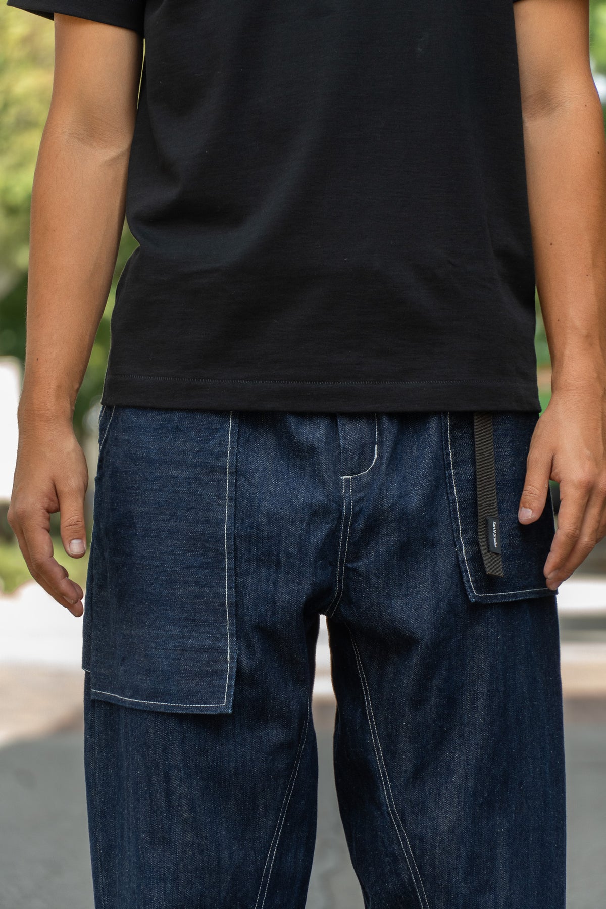 A close-up of a person wearing dark blue denim cargo pants with a black belt and a black t-shirt, photographed outdoors.