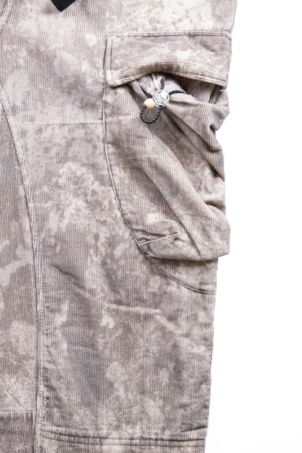 Close-up of a pair of cargo pants in a gray and beige camouflage pattern, showing a side pocket on a white background