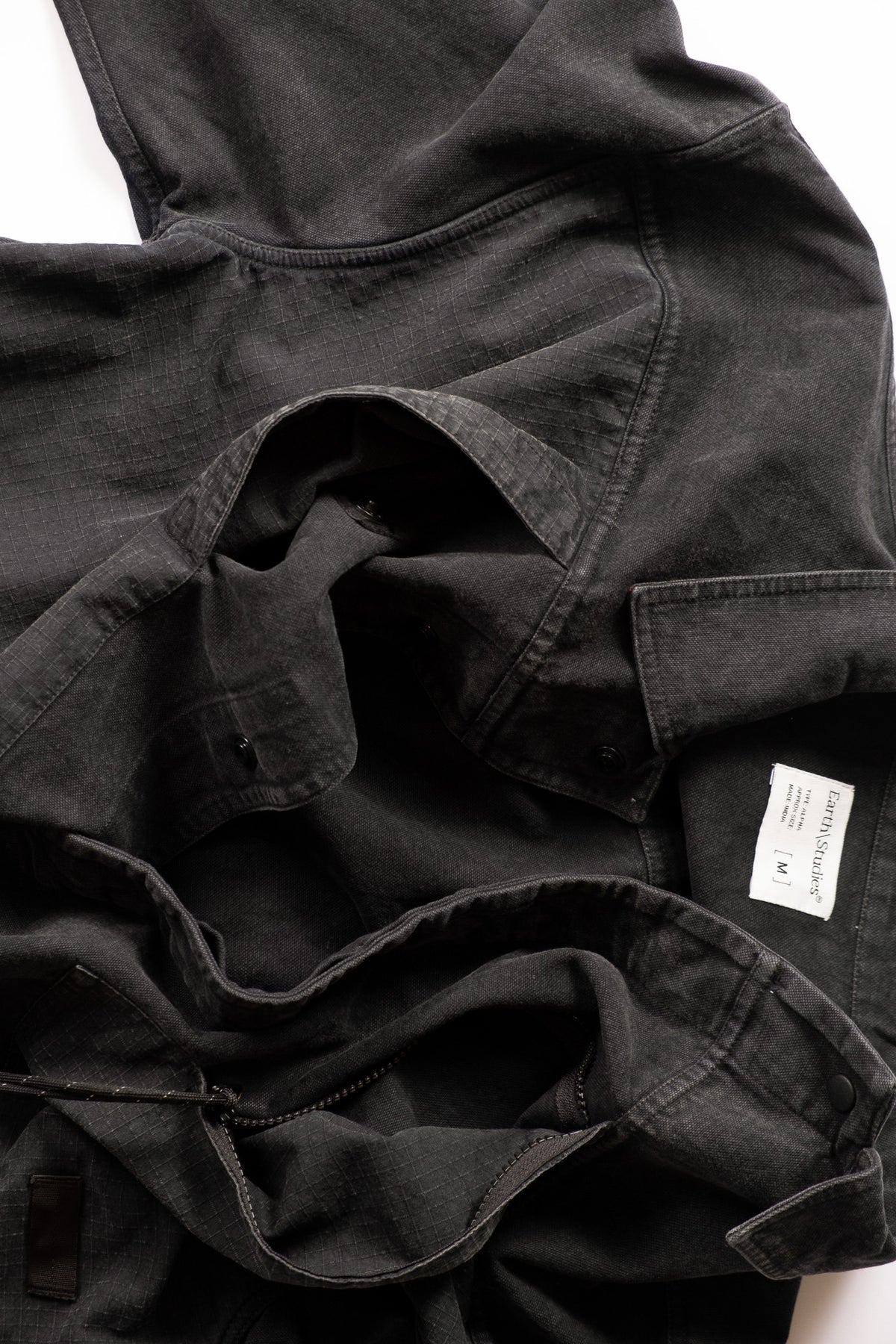 A close-up of a dark charcoal gray utility jacket with a flap pocket, laid flat on a white background.