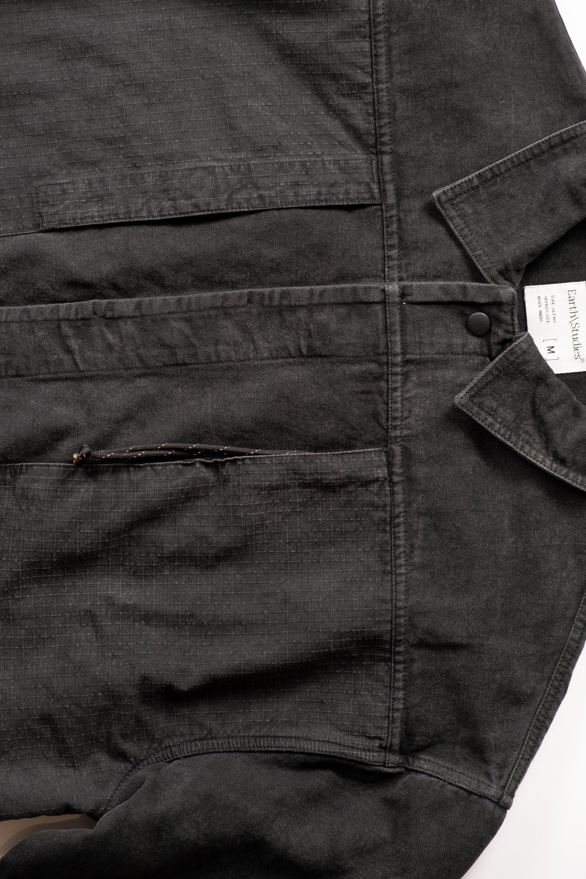 Close-up of a dark charcoal gray utility jacket, showing the fabric texture, and pocket details.