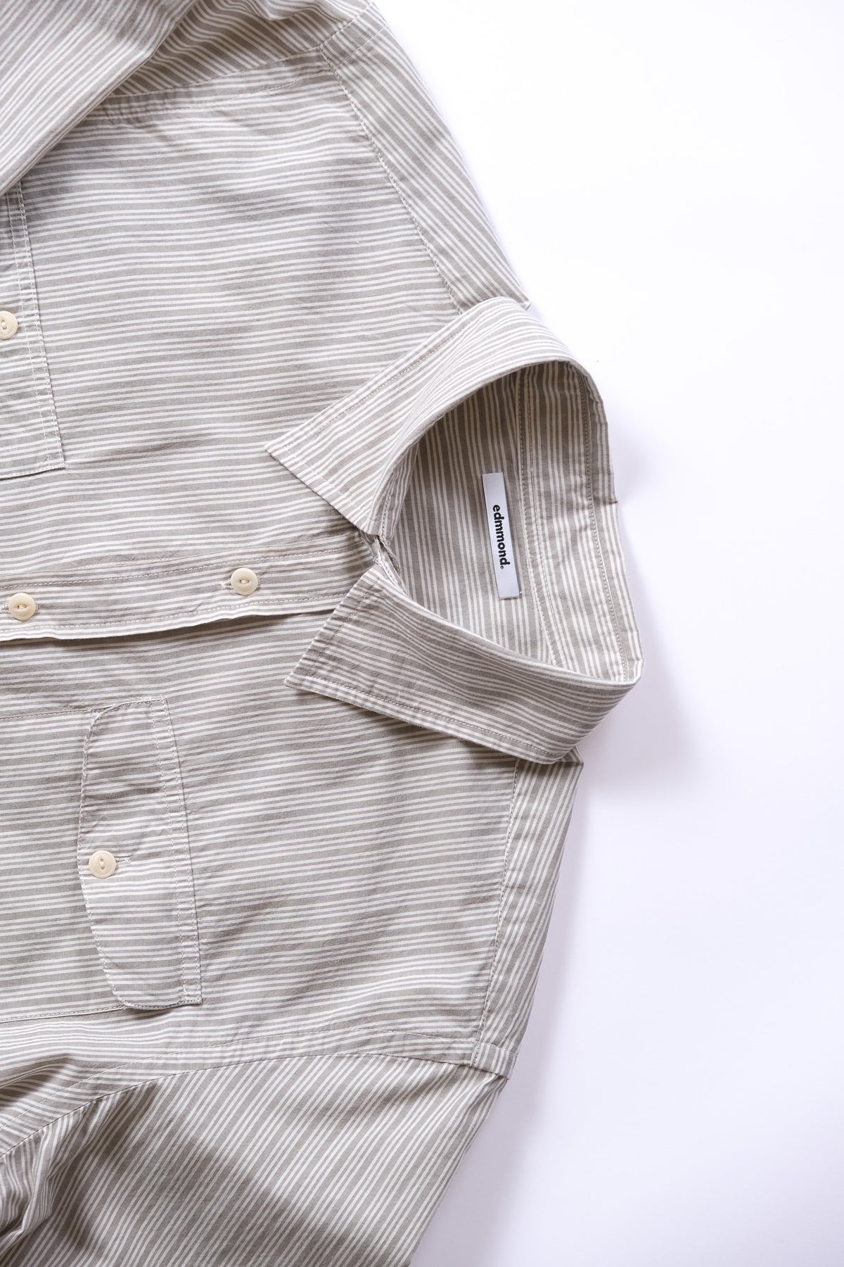Close-up of a light grey and white striped button-down shirt with a collar and chest pocket, laid flat on a white background.