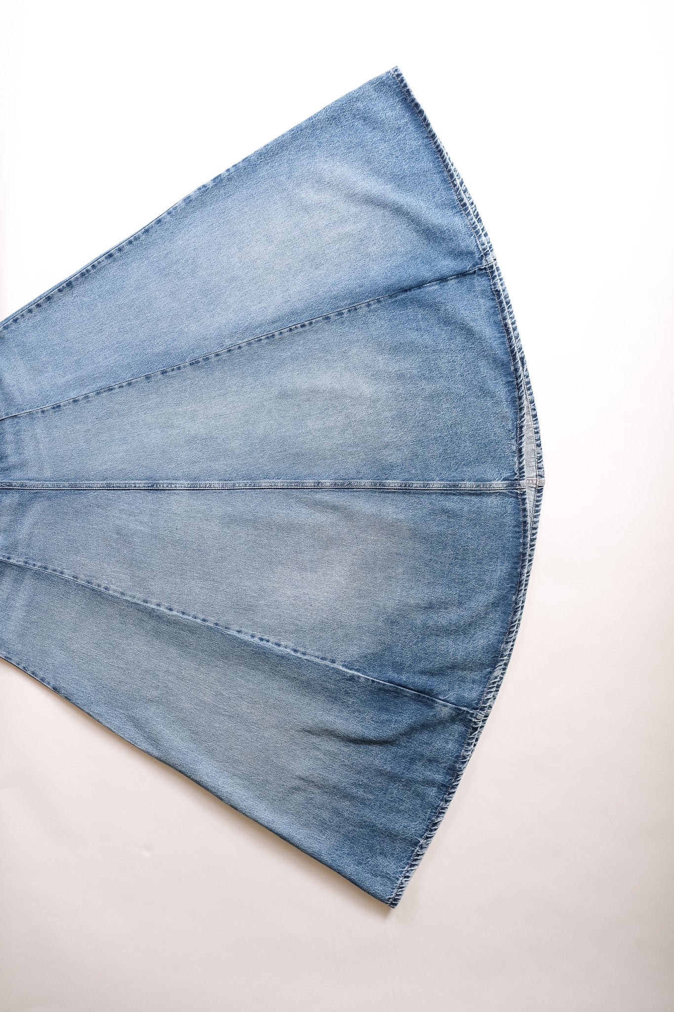 A close-up of a light blue denim fabric, showing the texture and stitching details, laid flat on a white background.