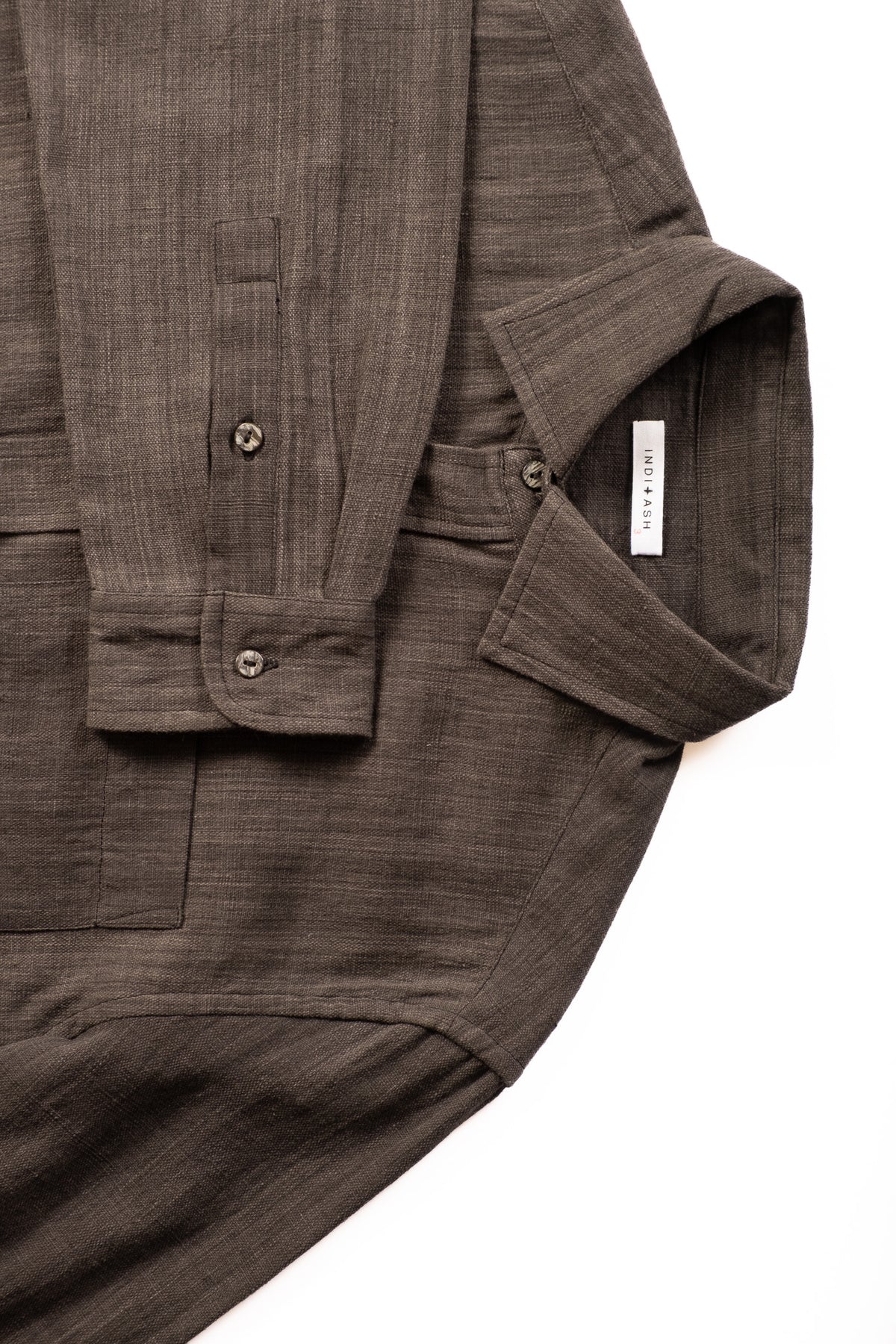 A close-up of a dark iron grey textured cotton shirt with a buttoned cuff and collar, laid flat on a white background.