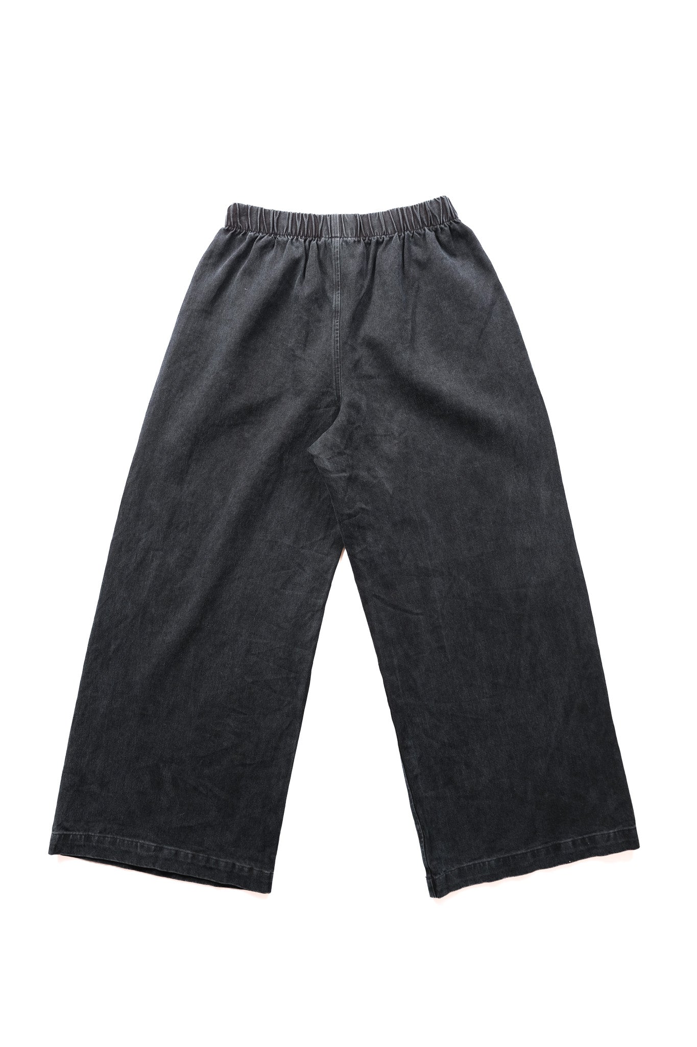A pair of black overdyed black wide-leg denim pants with an elastic waistband, laid flat against a white background.