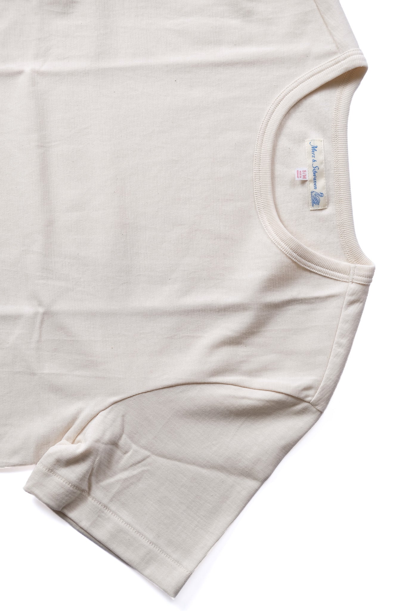 A close-up of a light beige cotton t-shirt showing the sleeve, collar, and inner neck label on a white background.