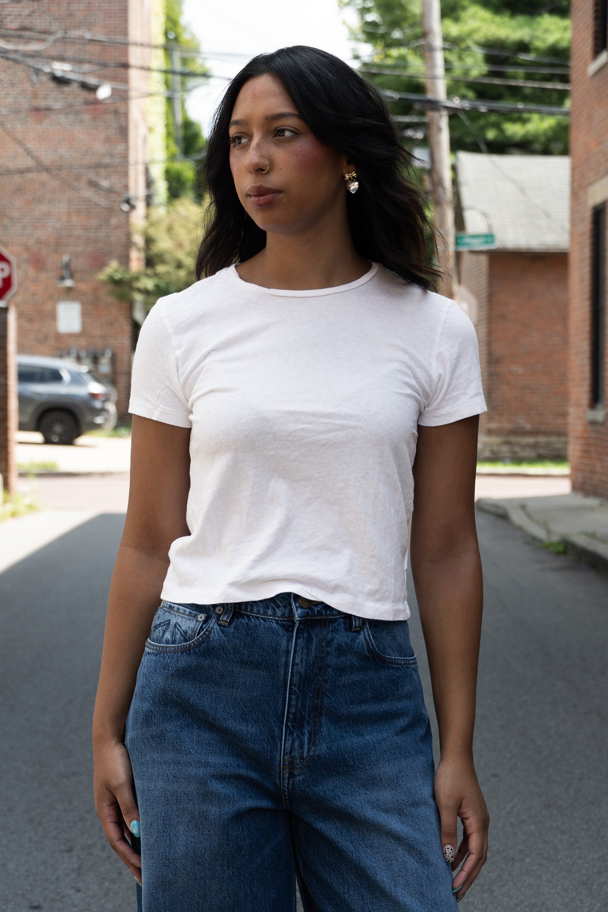 A woman wearing a plain white short-sleeve crewneck t-shirt and blue jeans standing in the street.