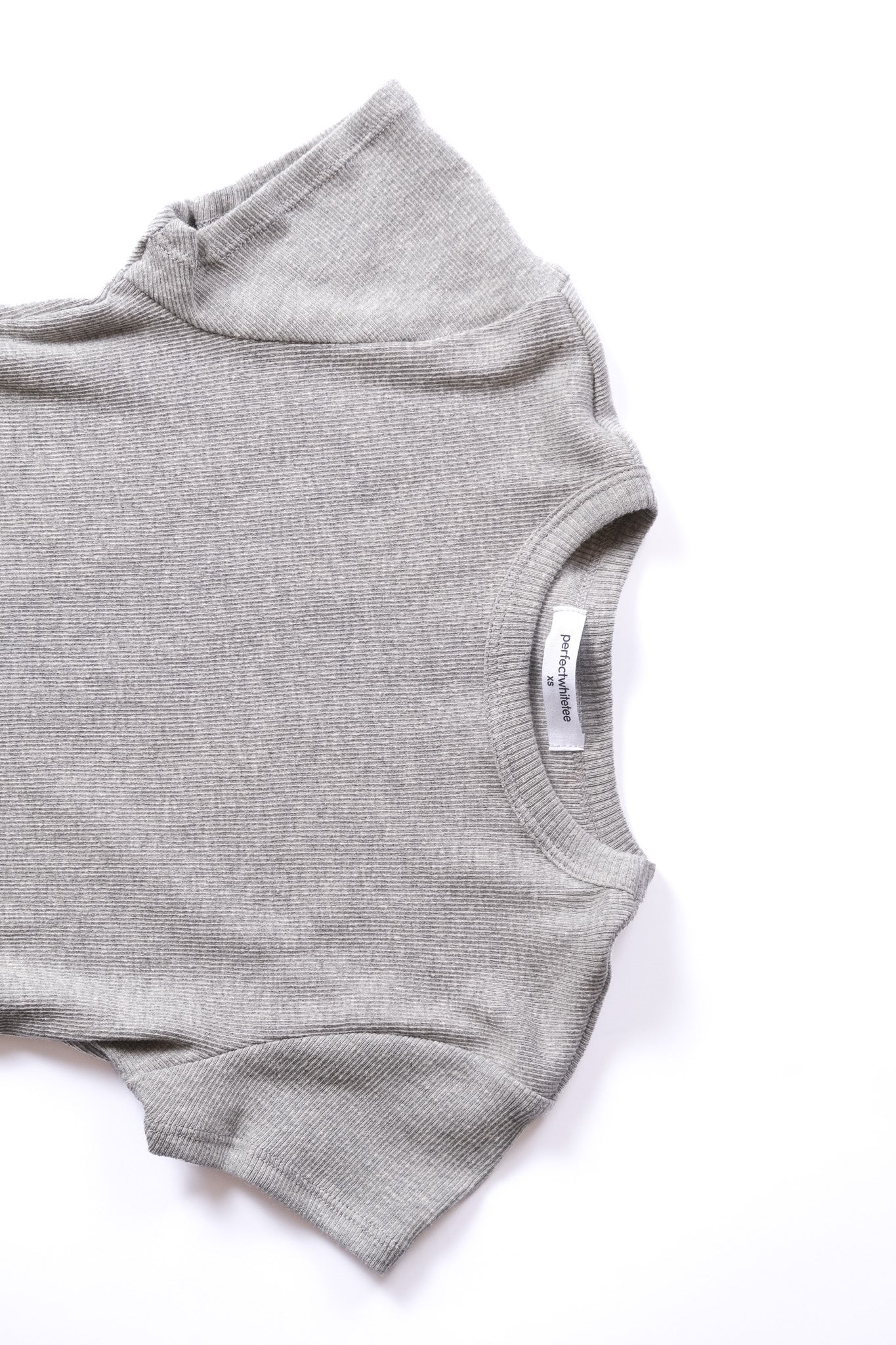 A close-up of a light gray ribbed knit tshirt laid flat on a white background, showing the sleeveless neckline and inner neck label.