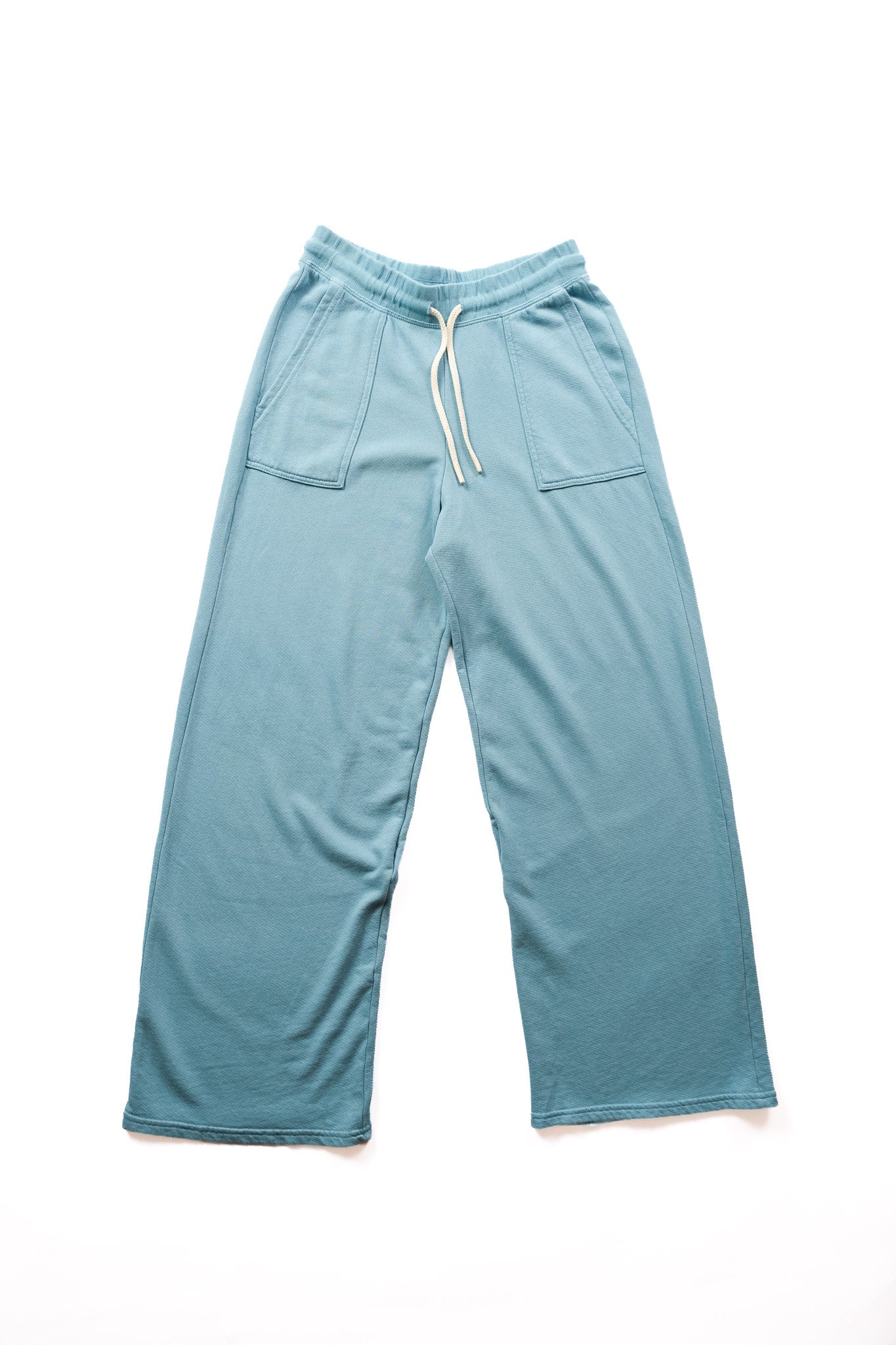 A pair of wide-leg lounge pants in a dusty teal blue color, featuring an elastic waistband with a white drawstring and two front patch pockets, laid flat on a white background.