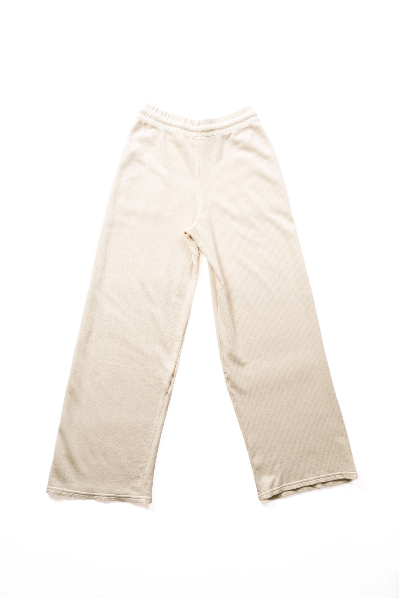 A pair of cream-colored cotton sweatpants with an elastic waistband viewed from the back laid flat against a solid white background.