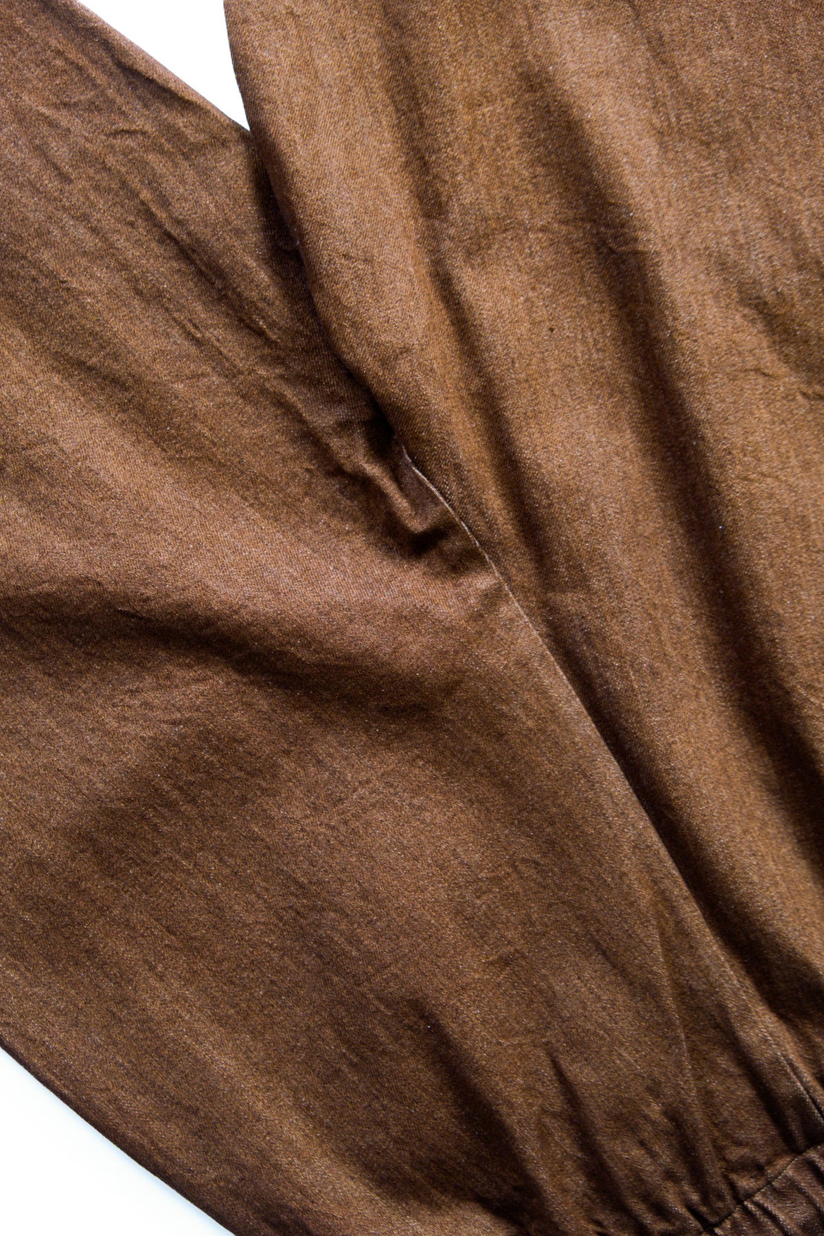A close-up of brown textured fabric with visible folds and a gathered seam.