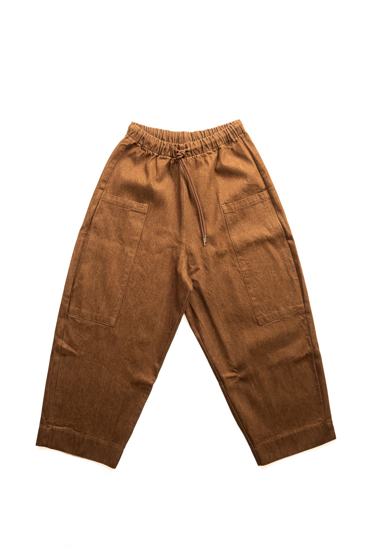 A pair of brown denim pants with an elastic waistband, drawstring, and large patch pockets, shown flat on a white background.