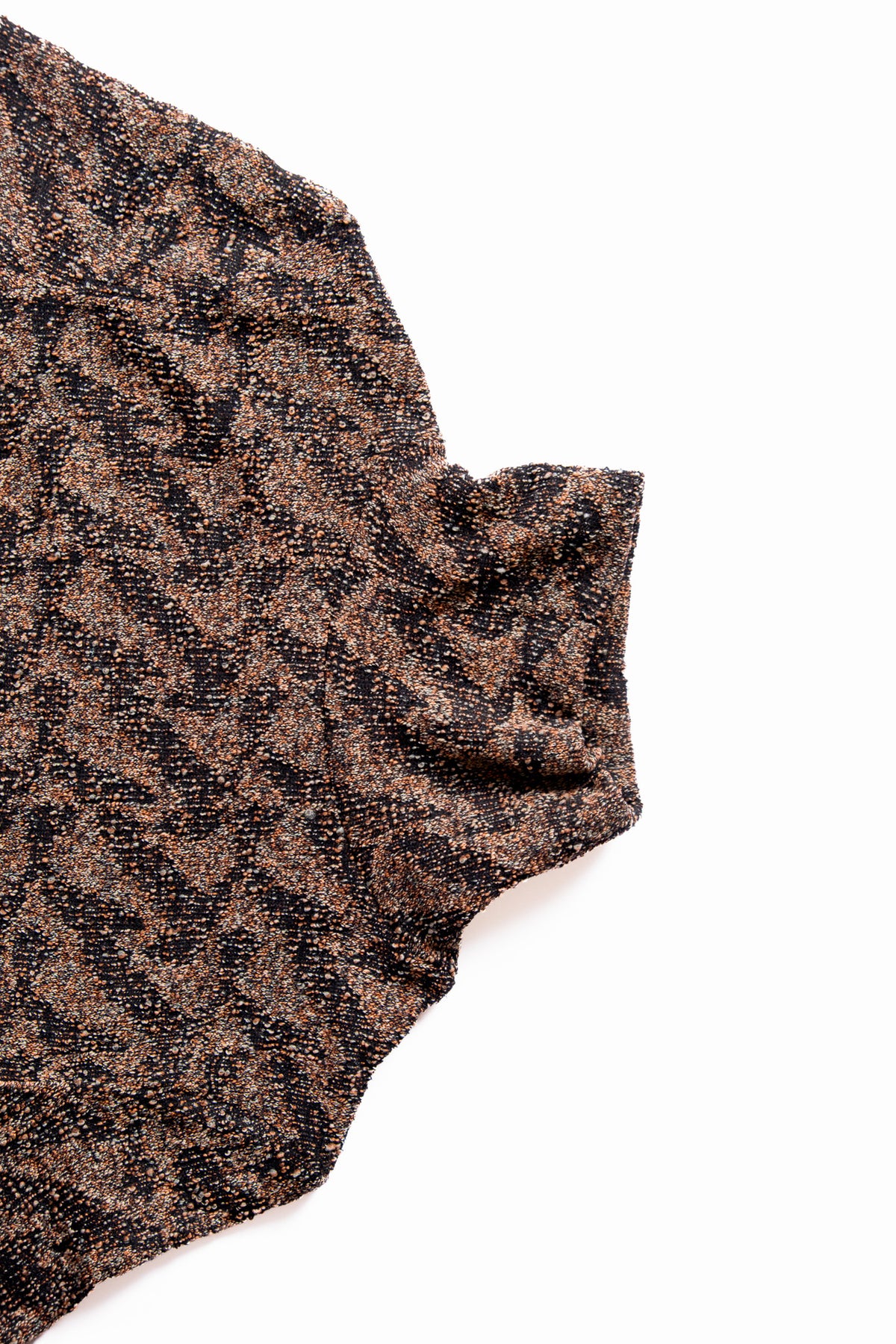 A close-up of a textured knit fabric with a mottled pattern of black and warm brown threads, on a solid white background.