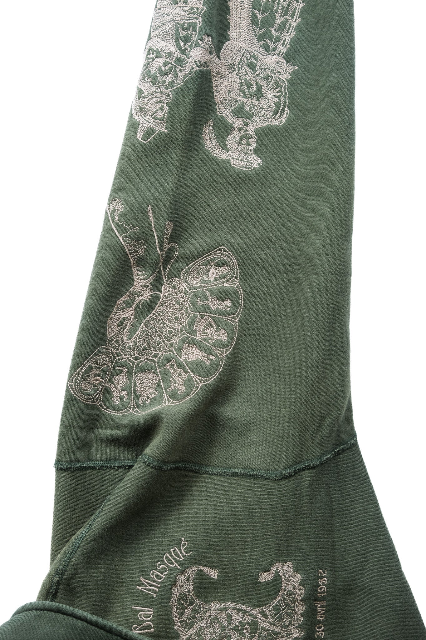 Close-up of an emerald green garment sleeve featuring an embroidered image of a hand holding a fan 