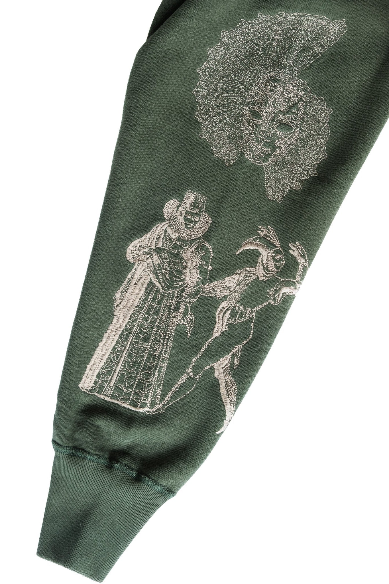 An emerald green sweatshirt sleeve featuring detailed white embroidered imagery shown against a plain white background.
