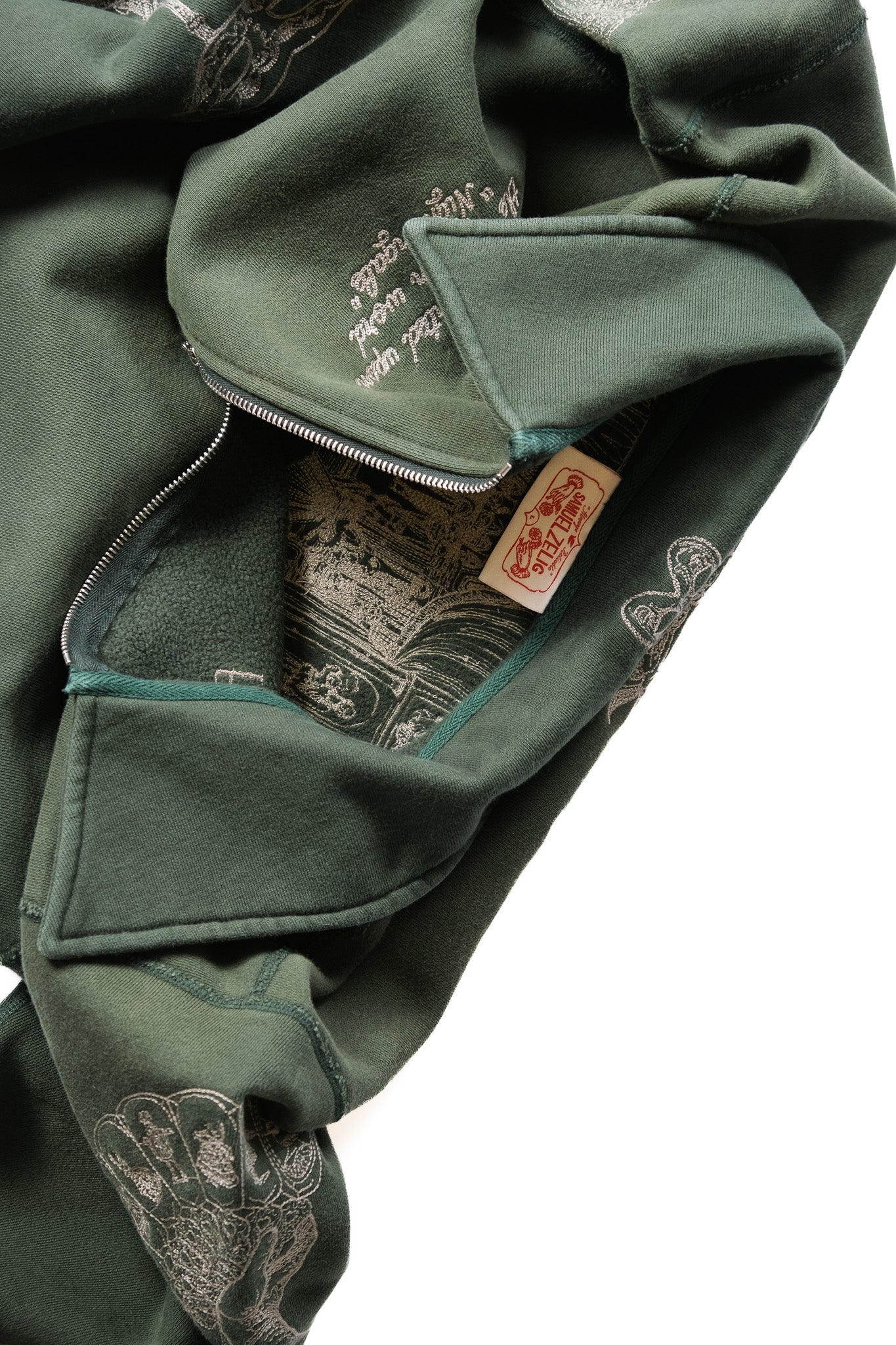 Close-up of an emerald green zippered hoodie with embroidery on the fabric and a visible brand tag.