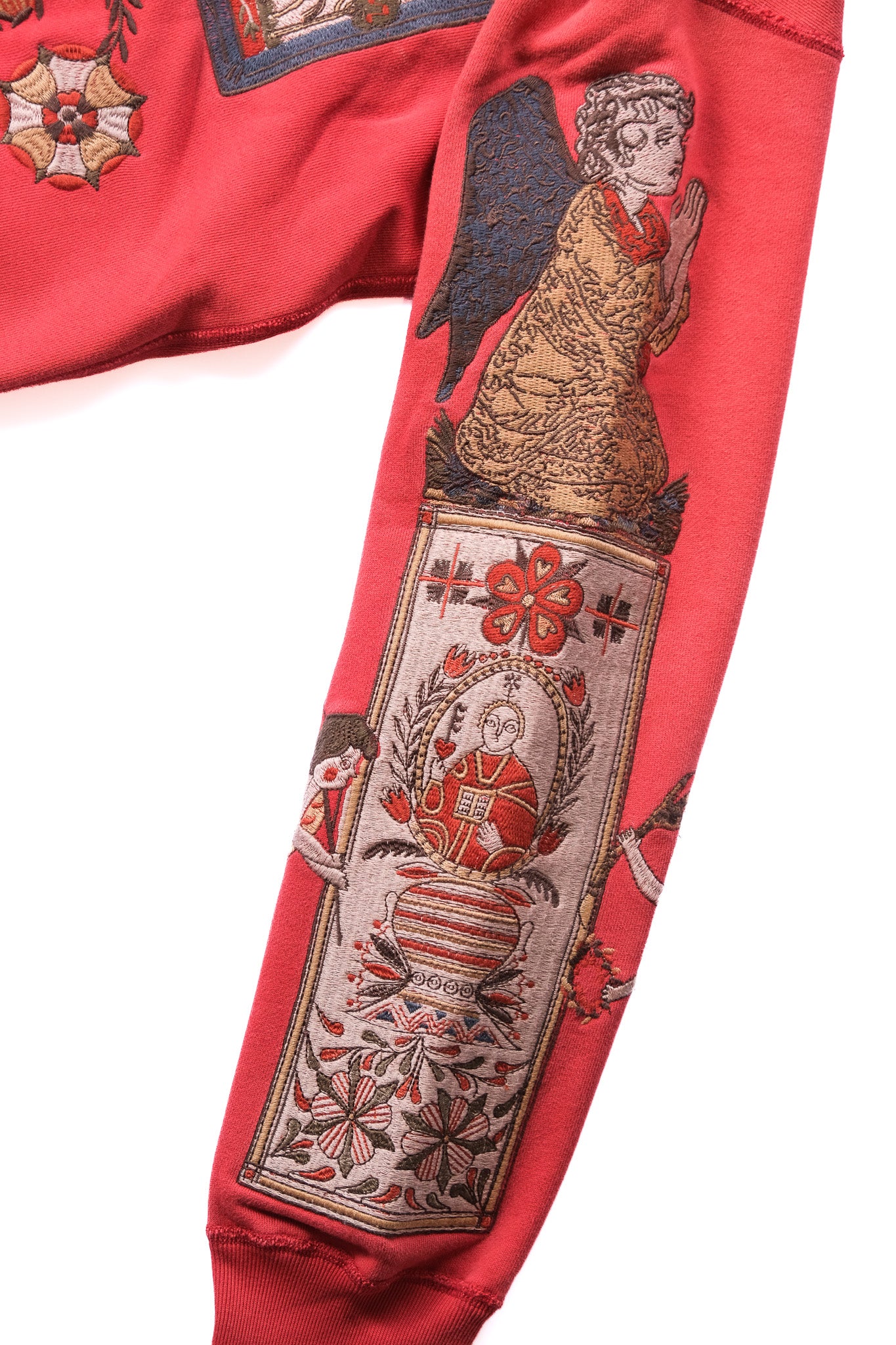 A close-up of a red sweatshirt sleeve featuring a large vintage-style angel and floral tapestry print on the upper arm.